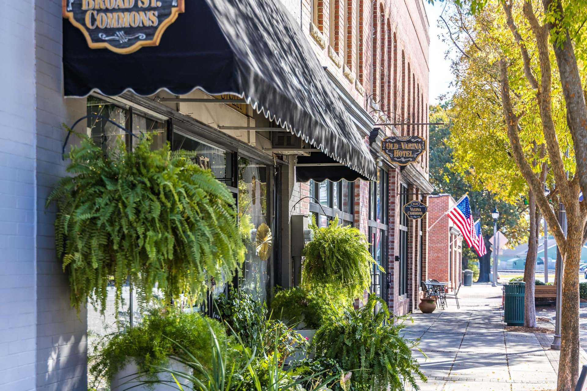 Charming brick storefronts on Broad Street in Fuquay-Varina NC with hanging ferns, awnings and American flag near Highland Forest