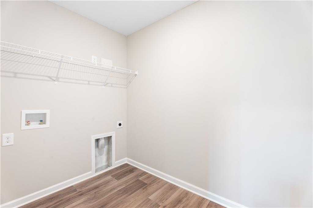 Spacious laundry room with wire shelving, washer/dryer hookups on beige walls and hardwood floors in Evermore Homes The Washington, Phenix City, AL