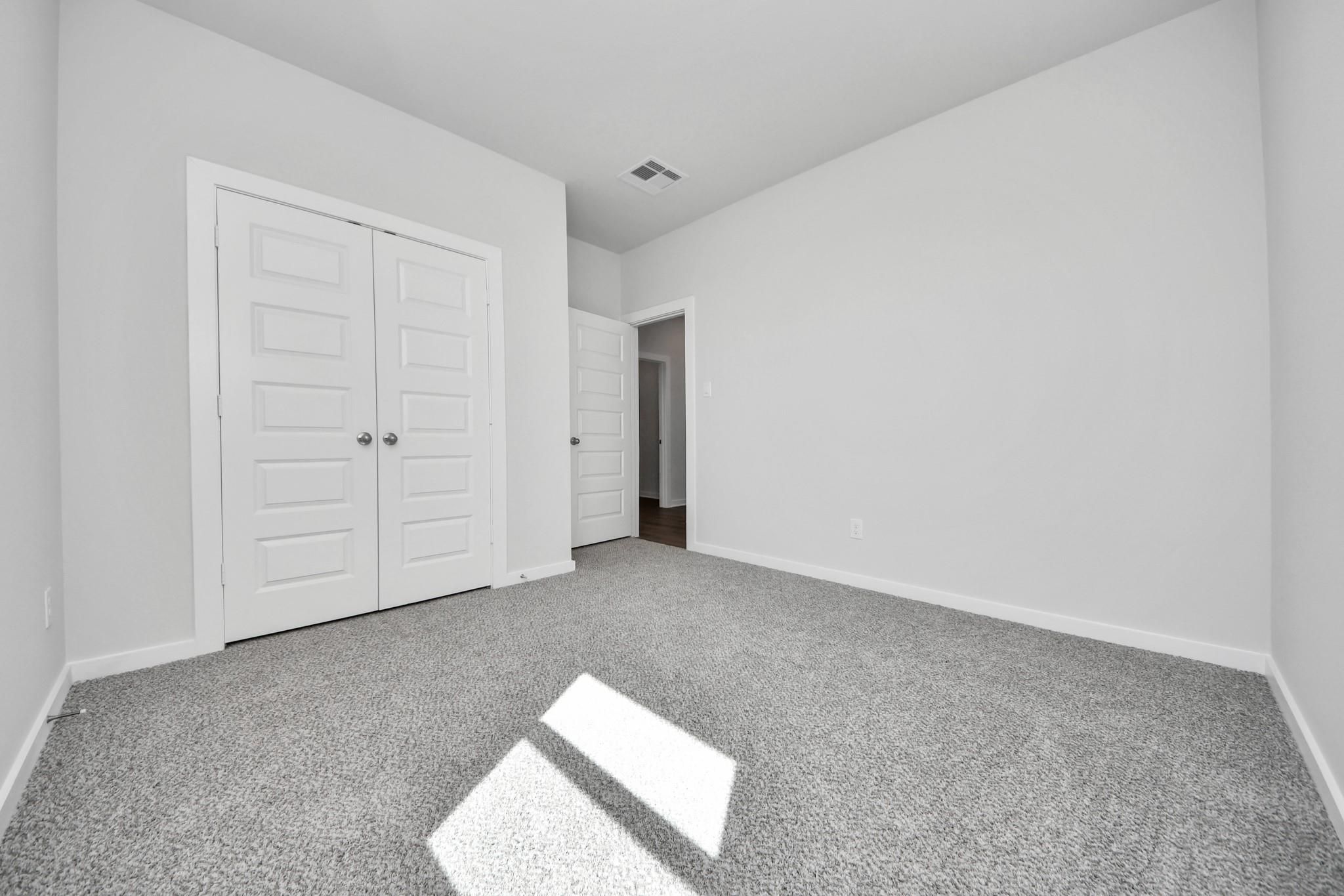 Bright secondary bedroom with plush carpet and closet in The Riviera A floor plan at Emberly in Beasley, Texas.