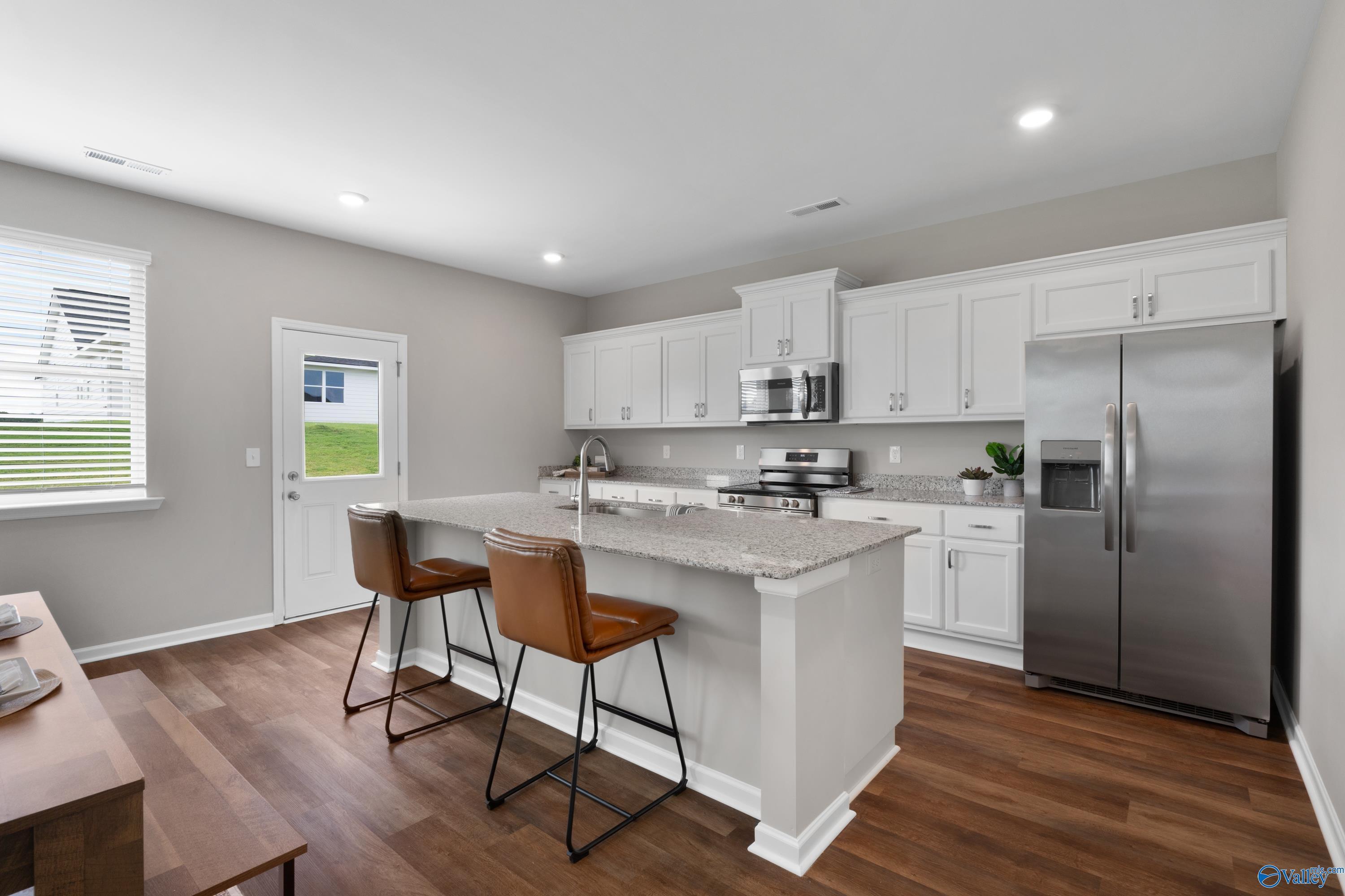 Modern kitchen with white shaker cabinets, granite island, stainless steel appliances in Evermore Homes The Noble, Madison AL