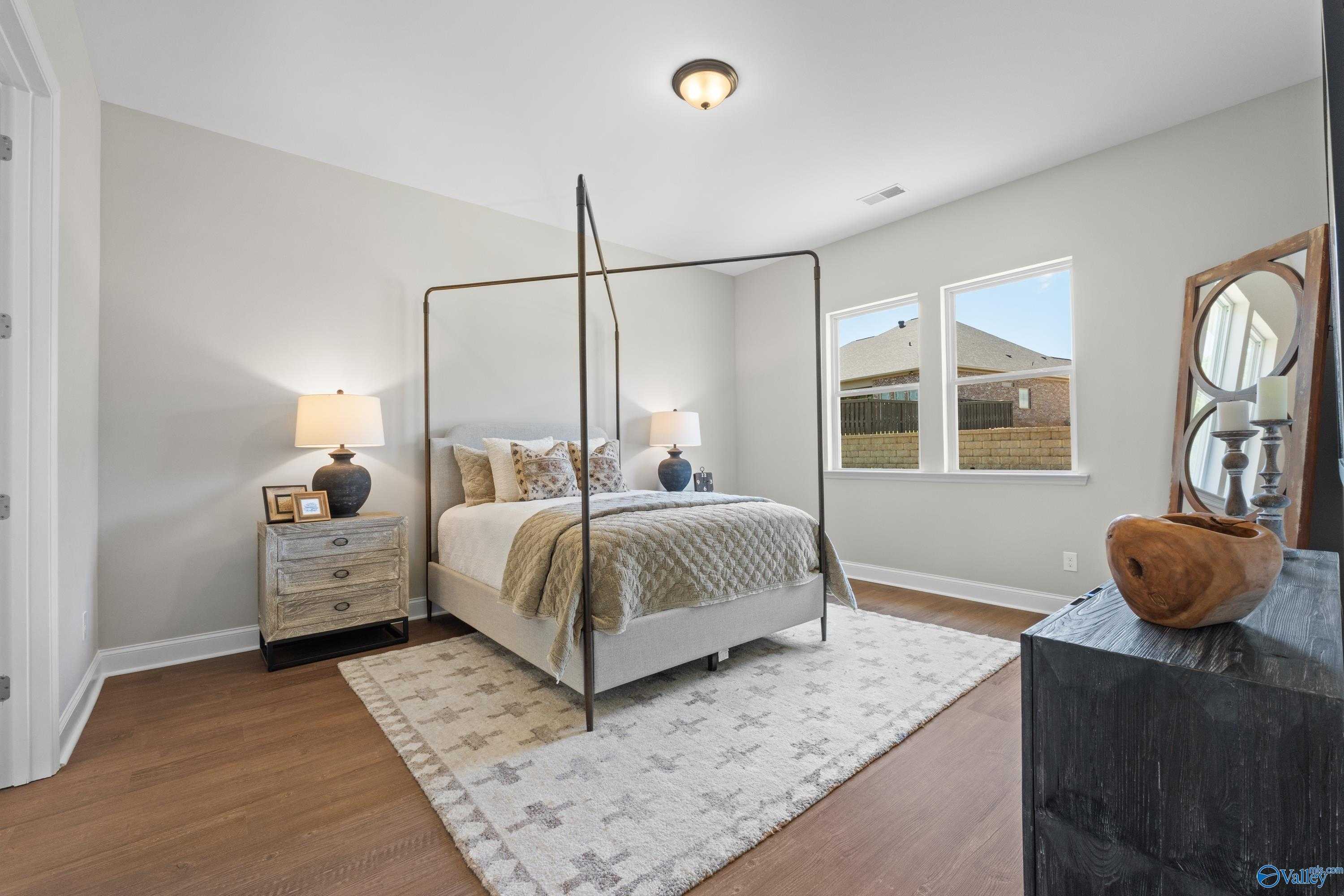 Elegant canopy king bed with neutral bedding, hardwood floors, and large windows in Evermore Homes The Haven bedroom, Owens Cross Roads, AL