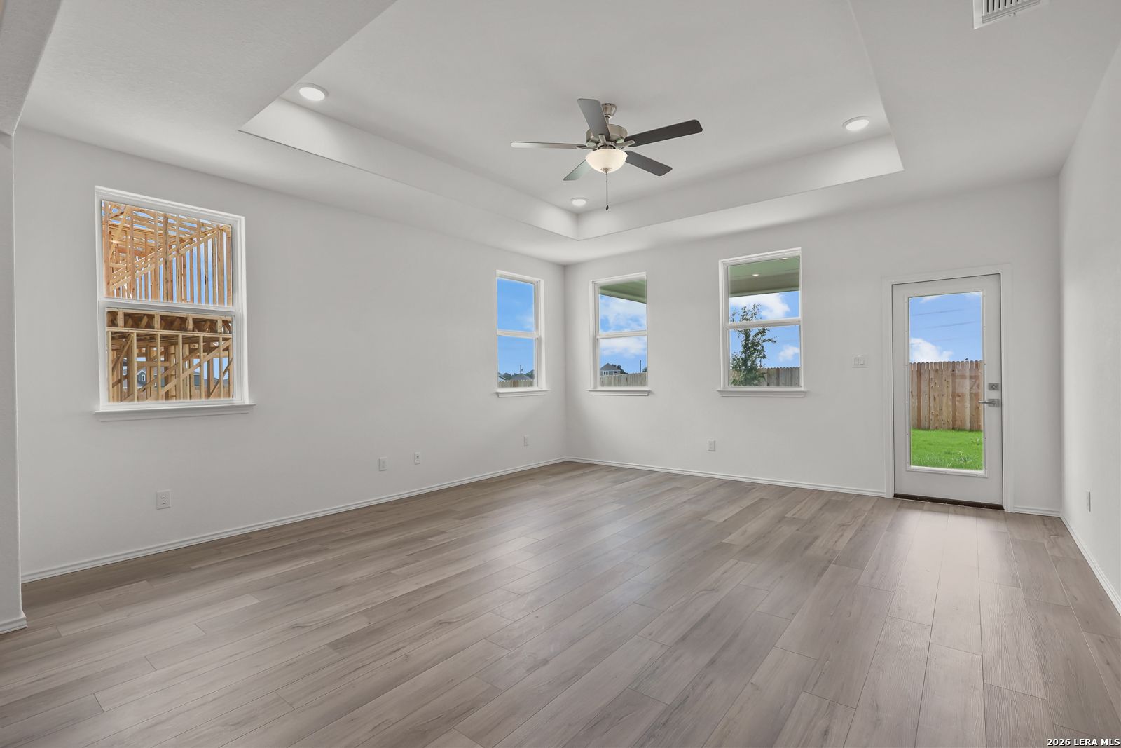 Spacious living room with tray ceiling, ceiling fan, large windows, and glass door to backyard in Davidson Homes The Glenwood E, Elmendorf, Texas