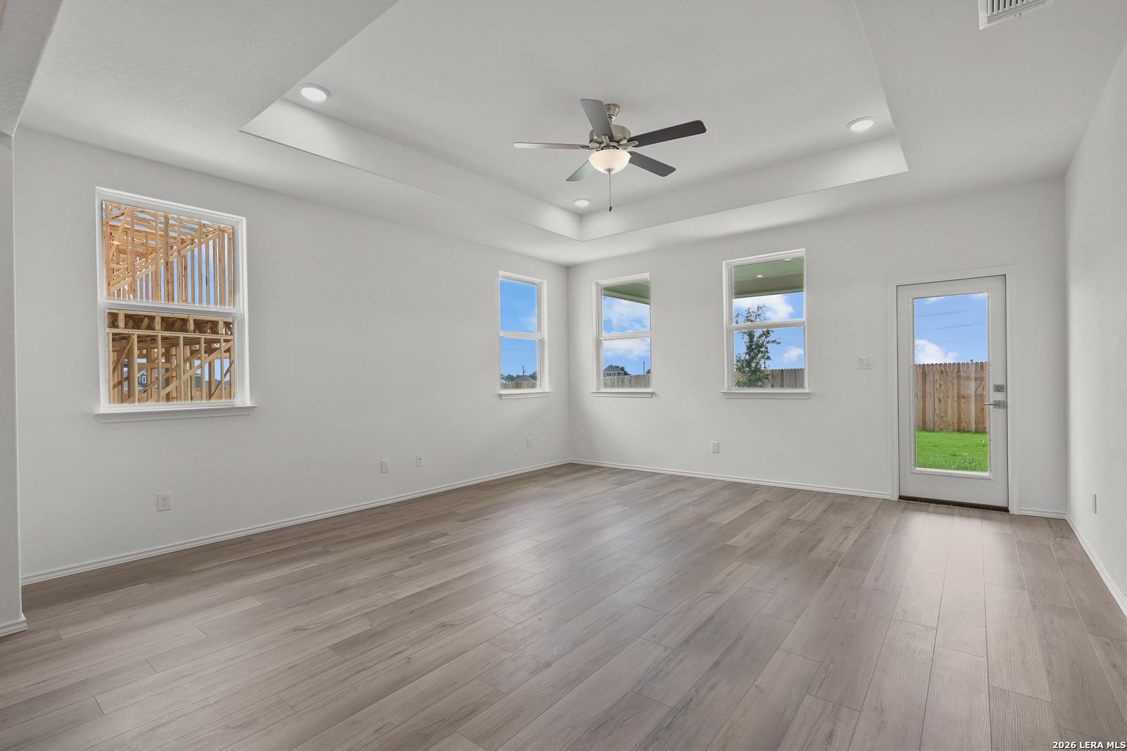 Spacious living room with tray ceiling, ceiling fan, large windows, and glass door to backyard in Davidson Homes The Glenwood E, Elmendorf, Texas