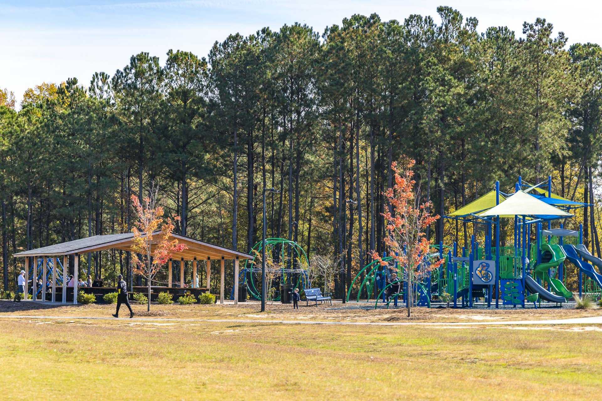 Vibrant playground with colorful slides and swings at Highland Forest in Fuquay-Varina NC, covered pavilion amid pine trees