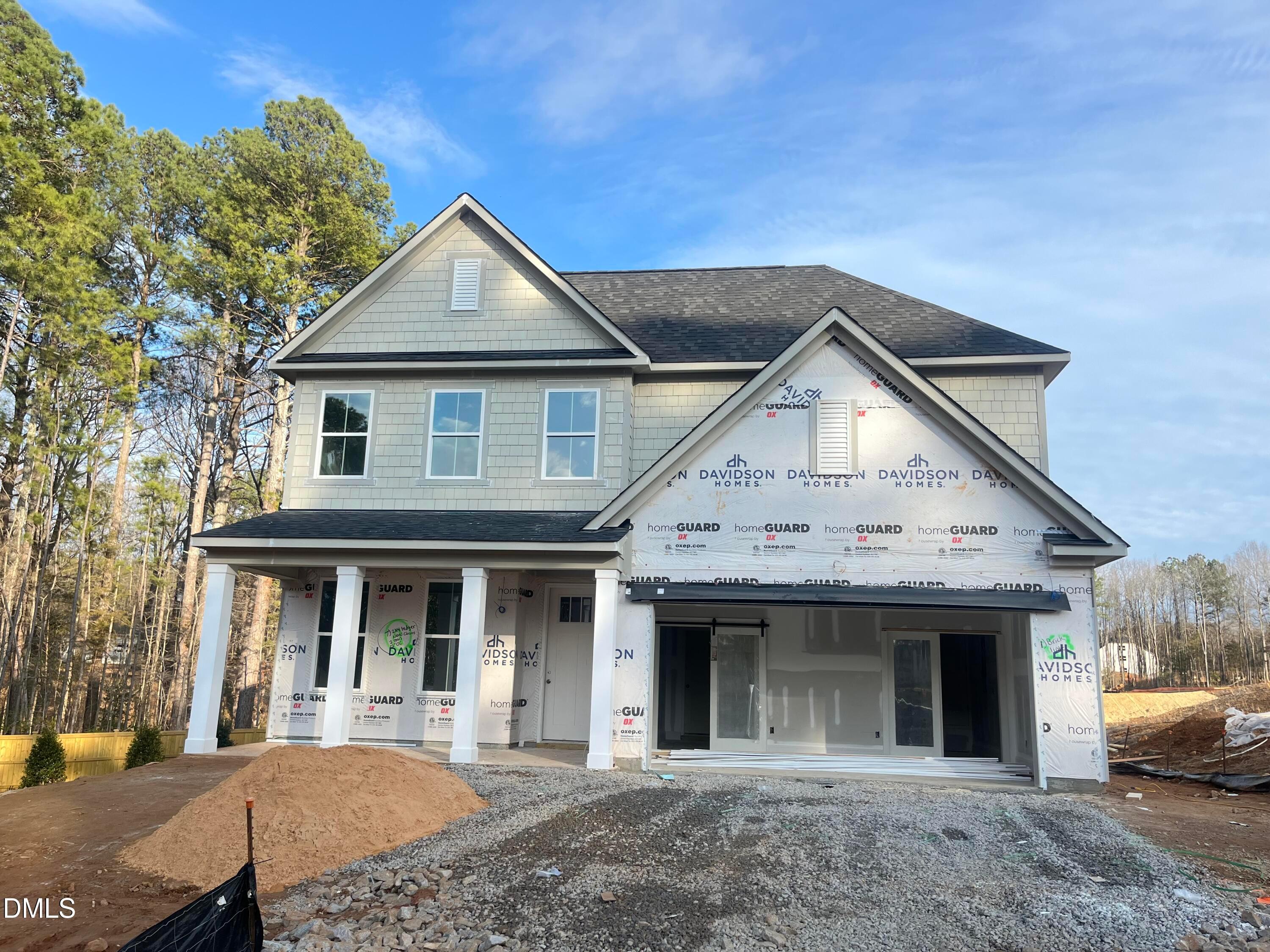 Two-story 5-bedroom home under construction featuring light gray siding, two-car garage, and columned front porch in Sage on North Main, Wake Forest, NC by Davidson Homes The Ashport G