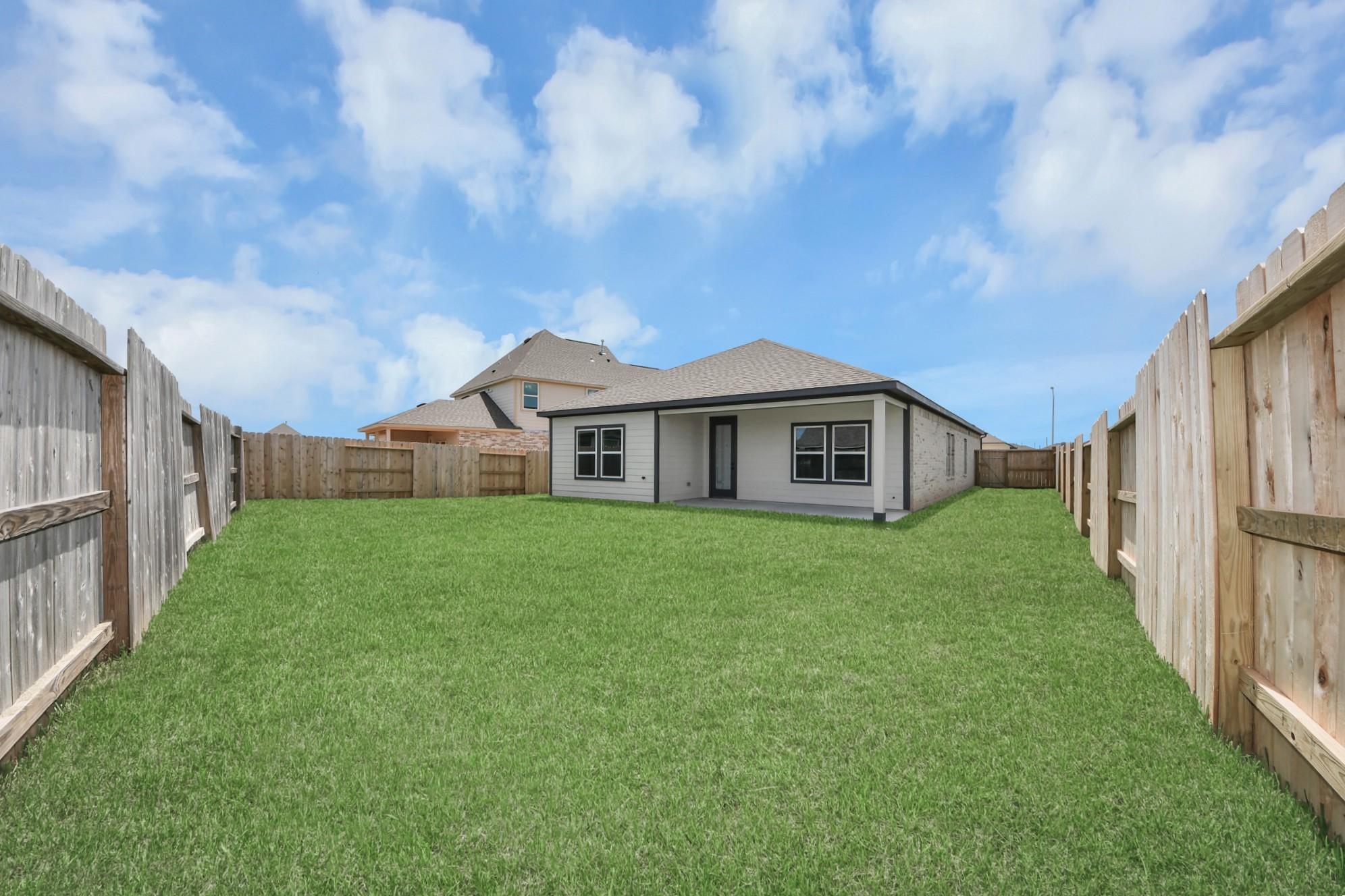 Private backyard with green lawn and wooden fence behind a 1-story Laguna C home in Sunterra, Katy, Texas.