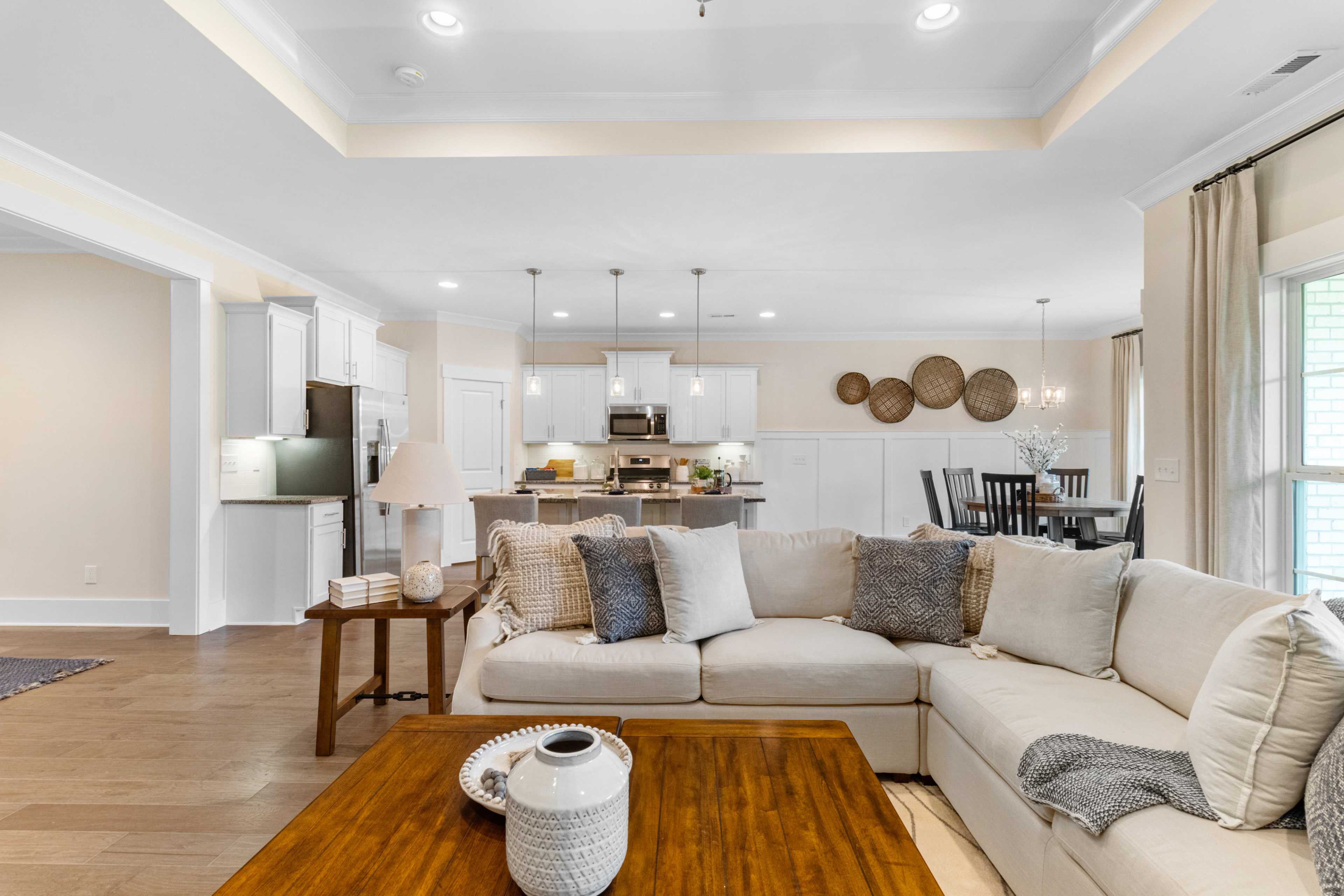Open-concept living room and kitchen in Noble Ridge Cullman AL by Davidson Homes with beige sectional sofa, hardwood floors, white cabinets