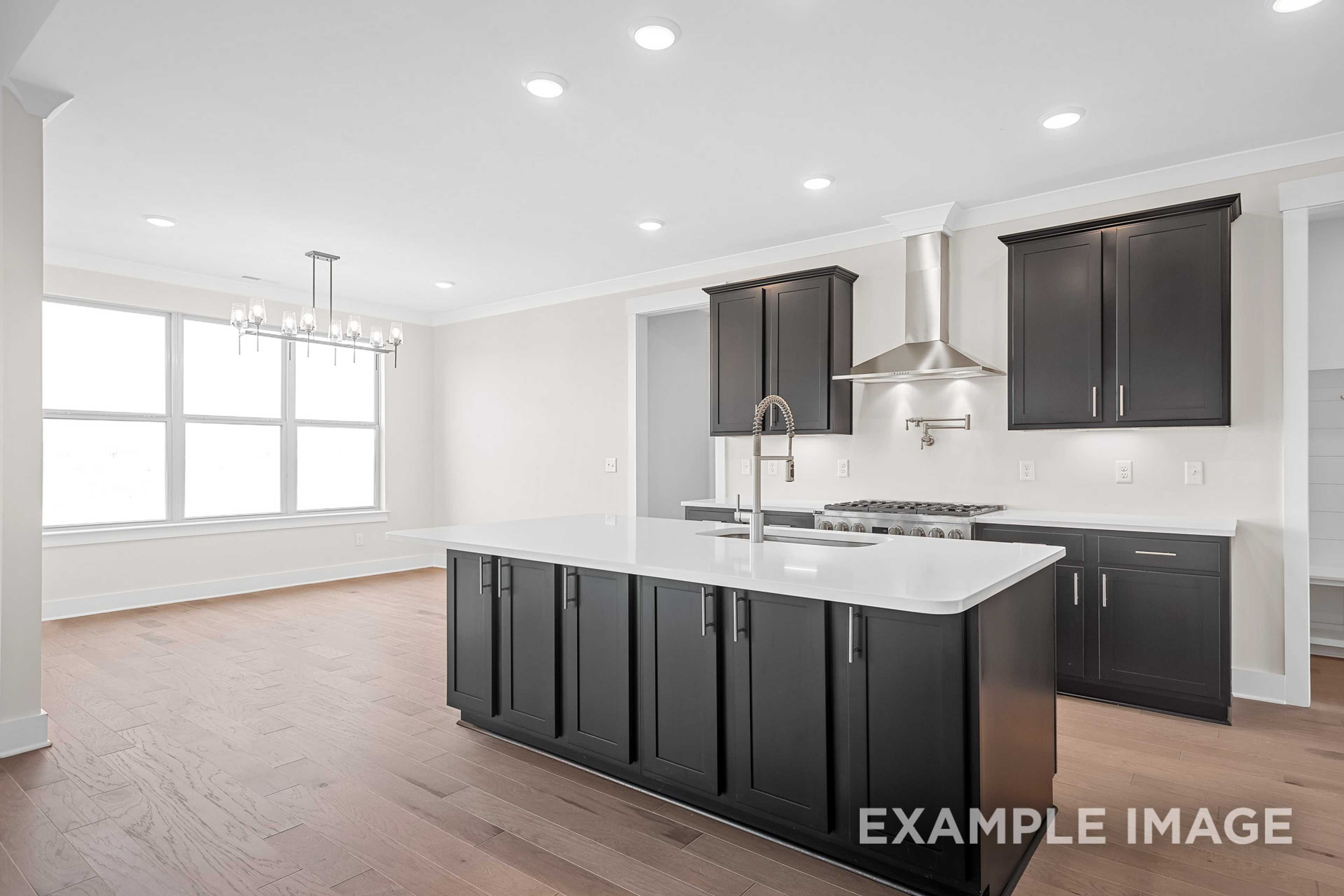 Spacious gourmet kitchen in The Hawkins with dark cabinets, large white island, gas range, and open layout