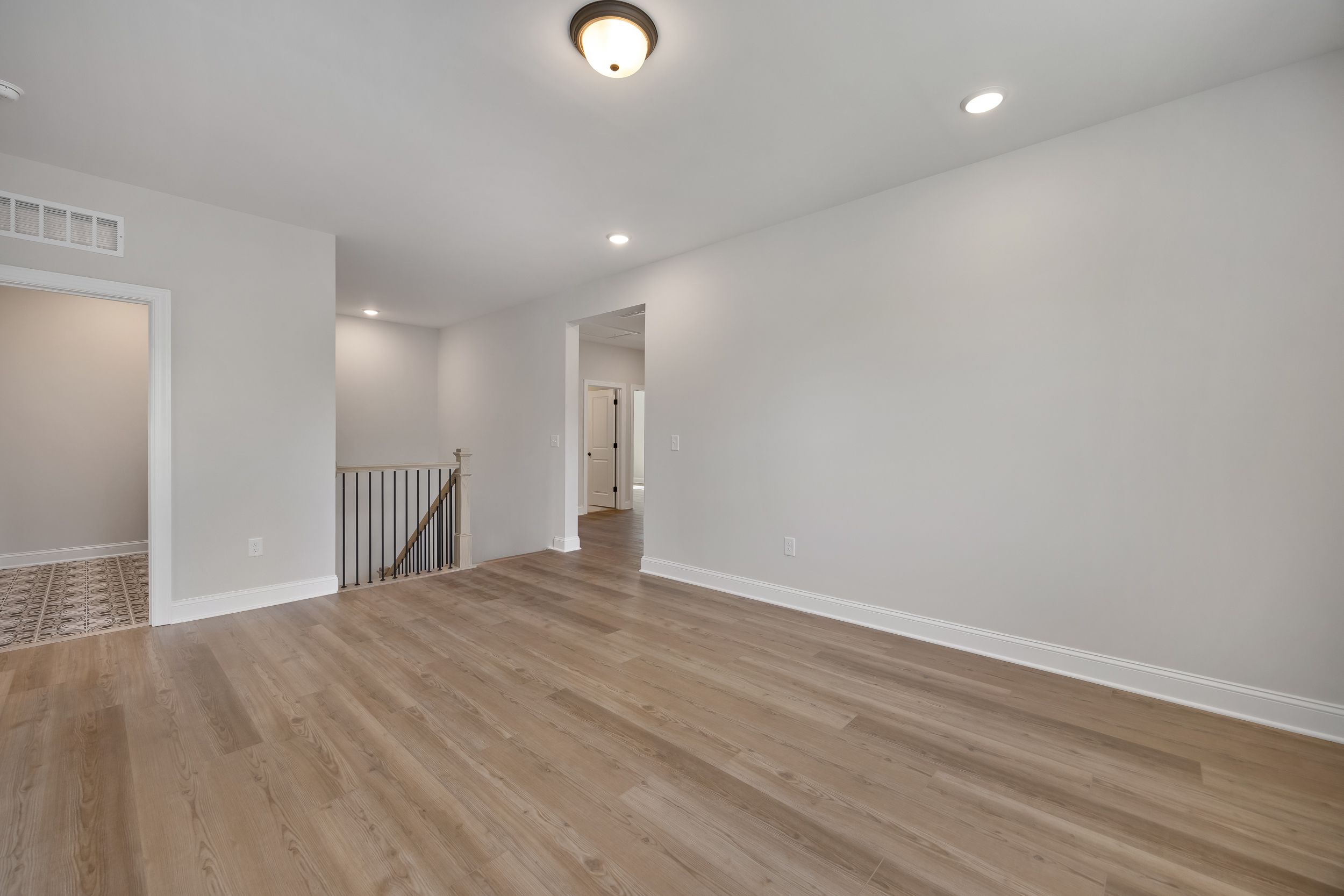 Bright upstairs hallway in Rockport Wake Forest NC home by Davidson Homes featuring hardwood floors and modern metal-railed staircase