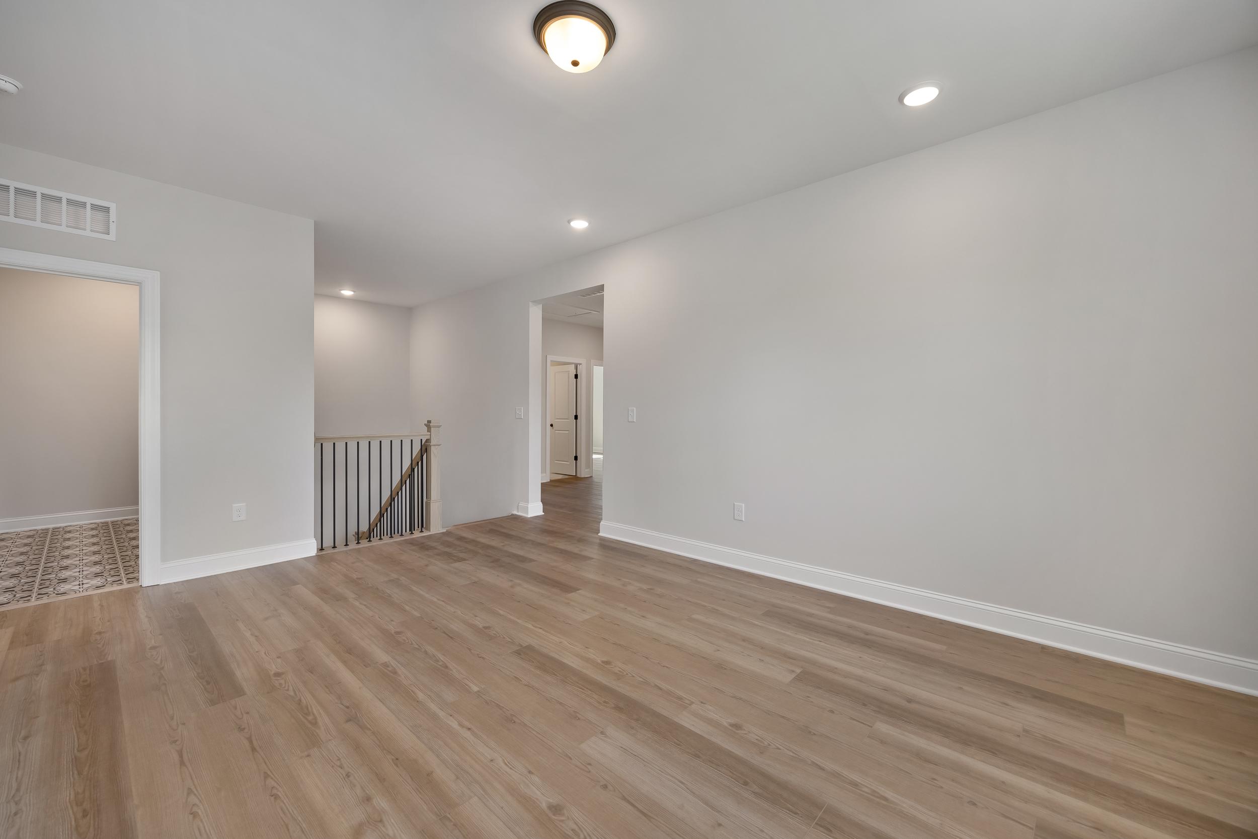 Bright upstairs hallway in Rockport Wake Forest NC home by Davidson Homes featuring hardwood floors and modern metal-railed staircase