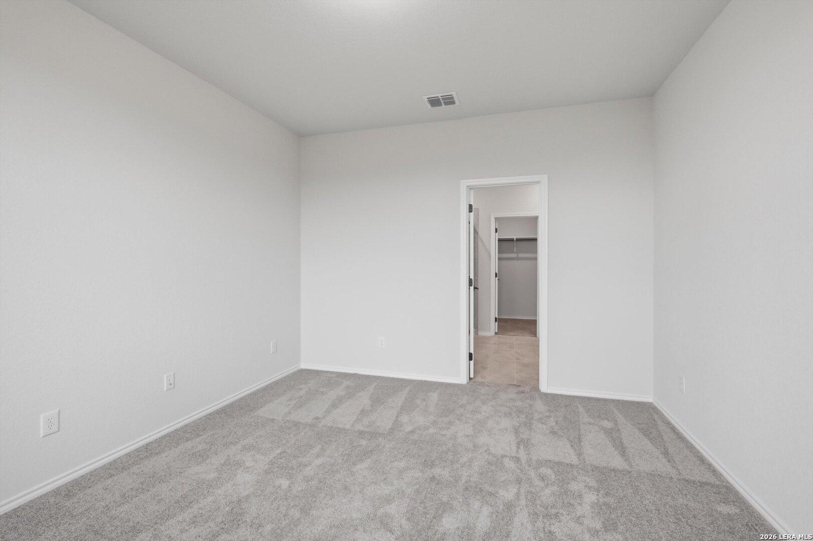Spacious empty bedroom with gray carpet, white walls, and walk-in closet in Davidson Homes The Blanco C, Agave, San Antonio