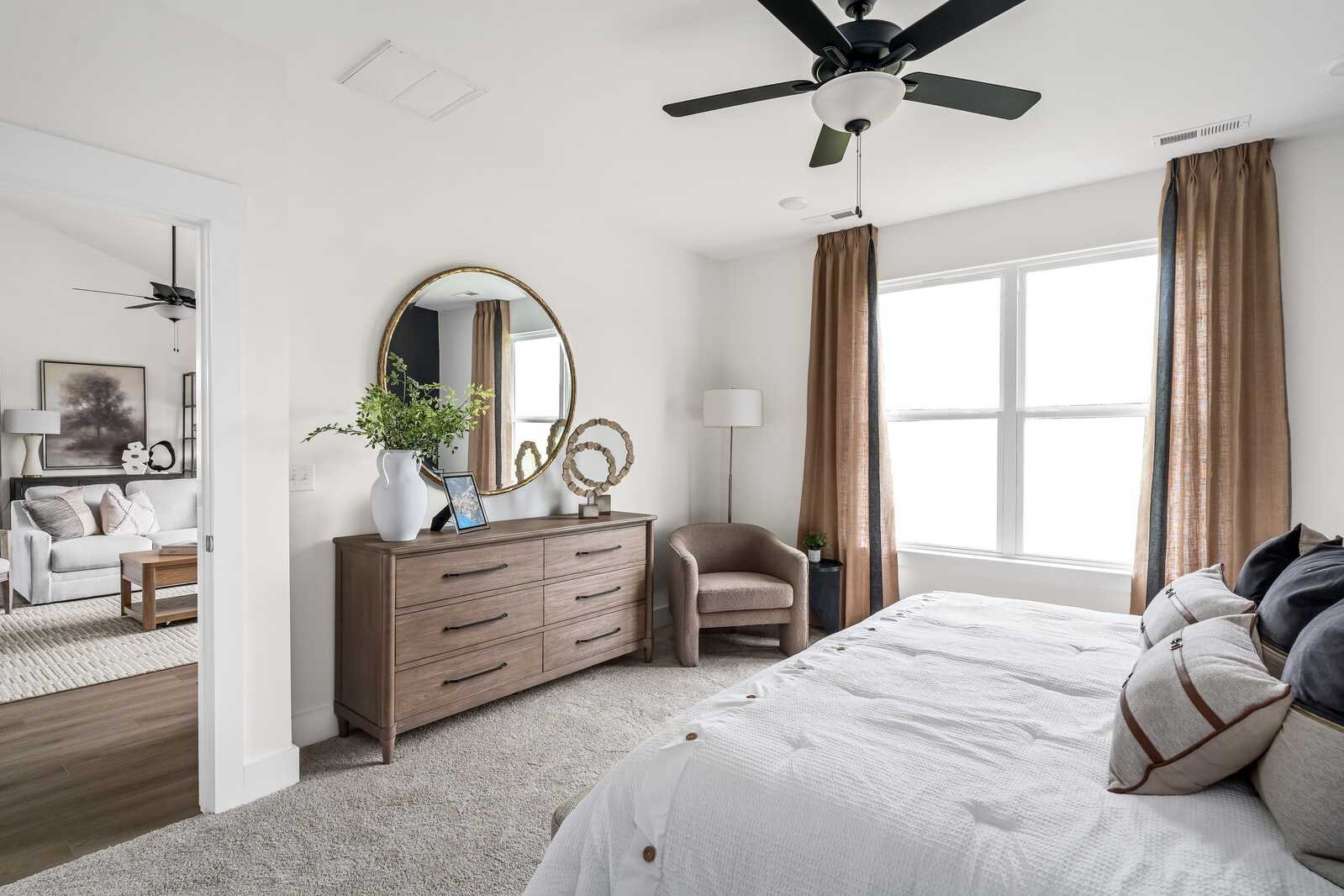 Spacious primary bedroom at Woods Crossing in Gallatin TN with king bed, wooden dresser, gold mirror, and draped windows