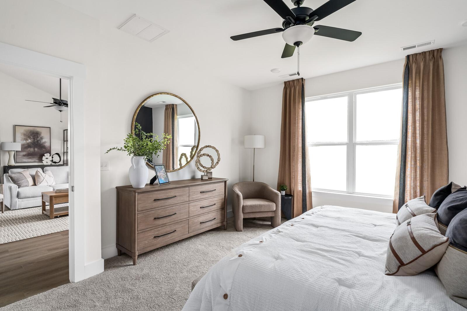 Spacious primary bedroom at Woods Crossing in Gallatin TN with king bed, wooden dresser, gold mirror, and draped windows