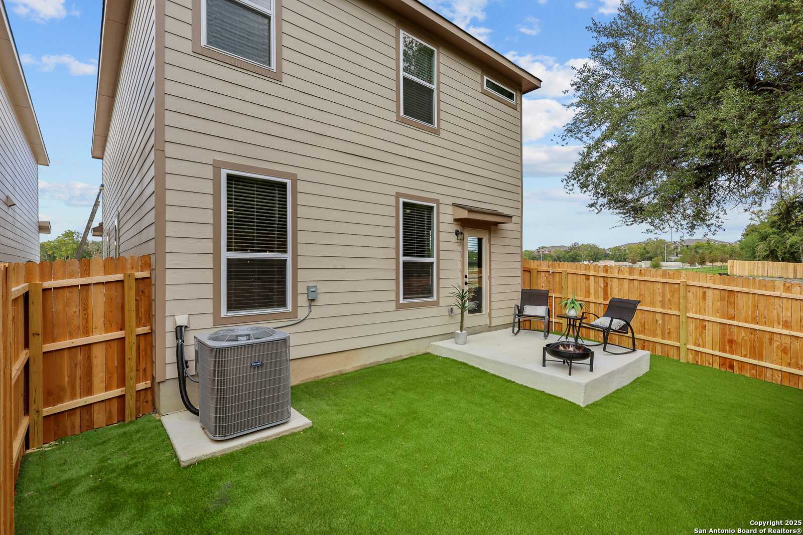 Private fenced backyard with covered patio, lounge chairs, and green turf lawn in Davidson Homes The Charlotte B, San Antonio, Texas