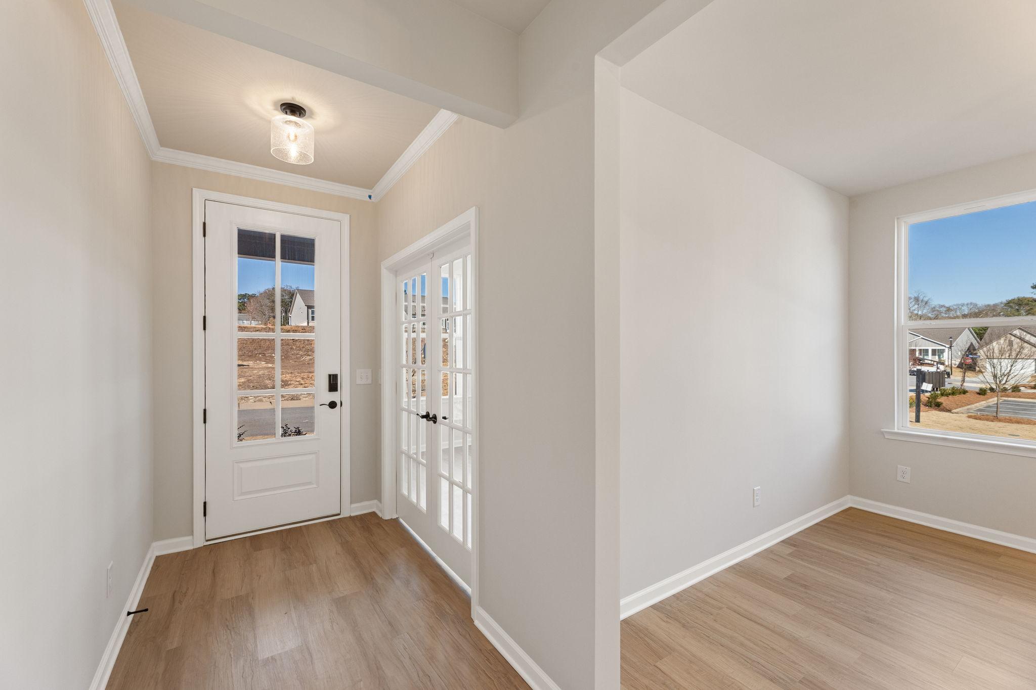 Bright entry foyer with glass-paneled front door, French doors, and hardwood floors in Davidson Homes The Glenwood C, Loganville, GA