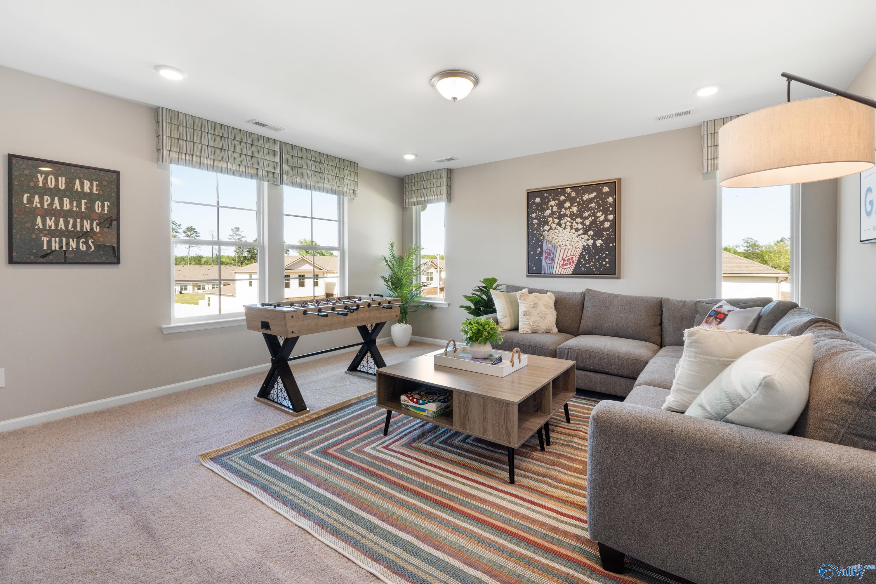 Cozy family room with gray sectional sofa, foosball table, motivational art, and neighborhood views in Davidson Homes The Stella, Madison AL