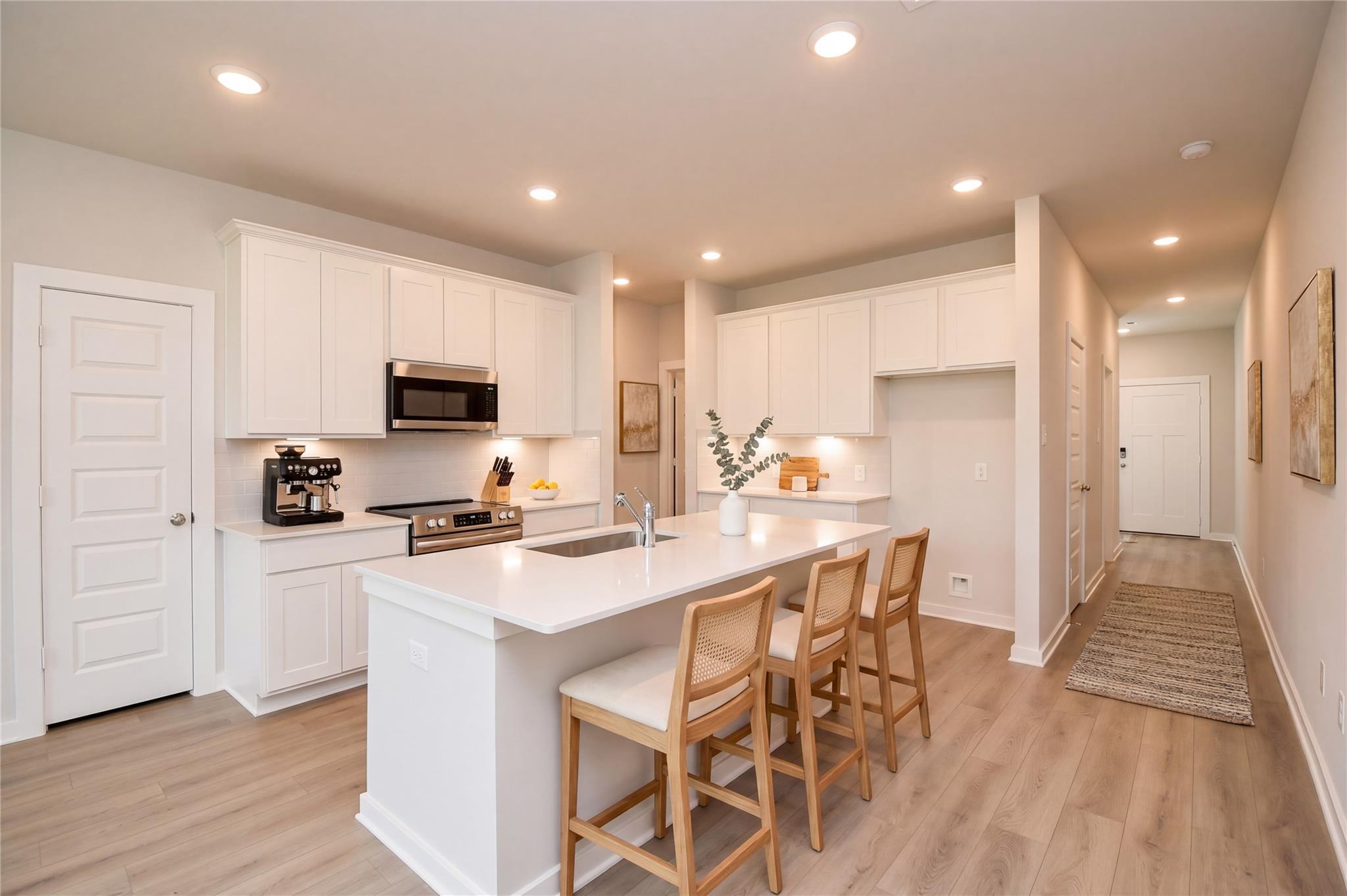White kitchen island with sink and barstool seating, stainless appliances, and wood-look floors in Davidson Homes The Frio F plan.