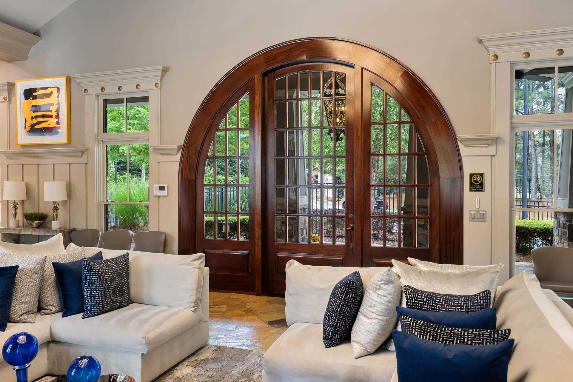 Grand arched wooden doors in open living room at The Village at Towne Lake, Woodstock GA with white sofas, blue pillows and large windows