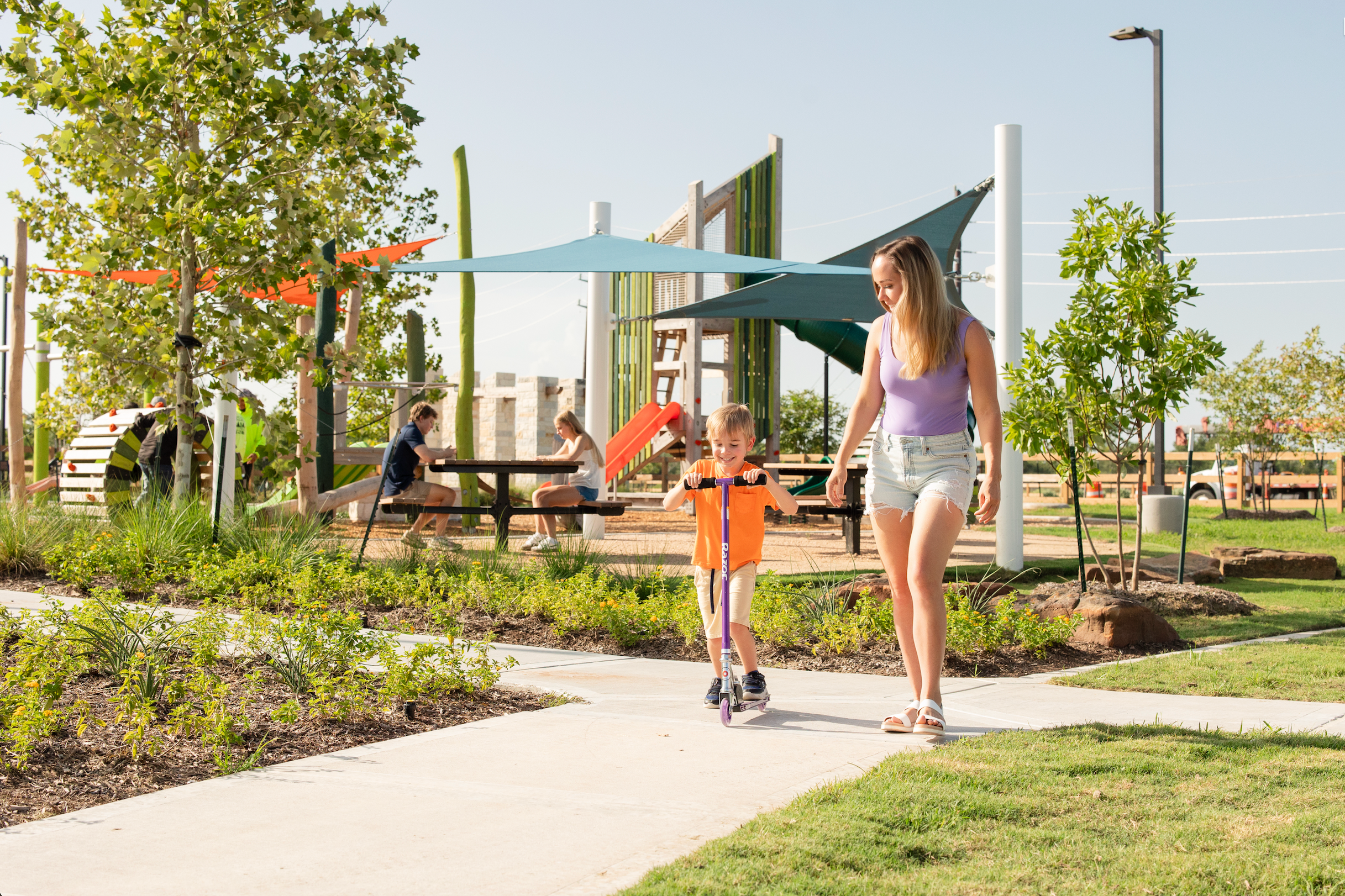 Mother and child scooting through shaded playground at Emberly in Beasley Texas with colorful play structures