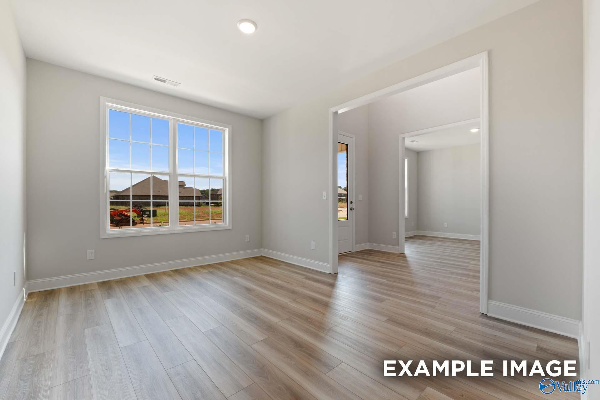 Bright bedroom with large window overlooking green yard, light gray walls, and hardwood floors in Davidson Homes The Madison A, Toney, Alabama