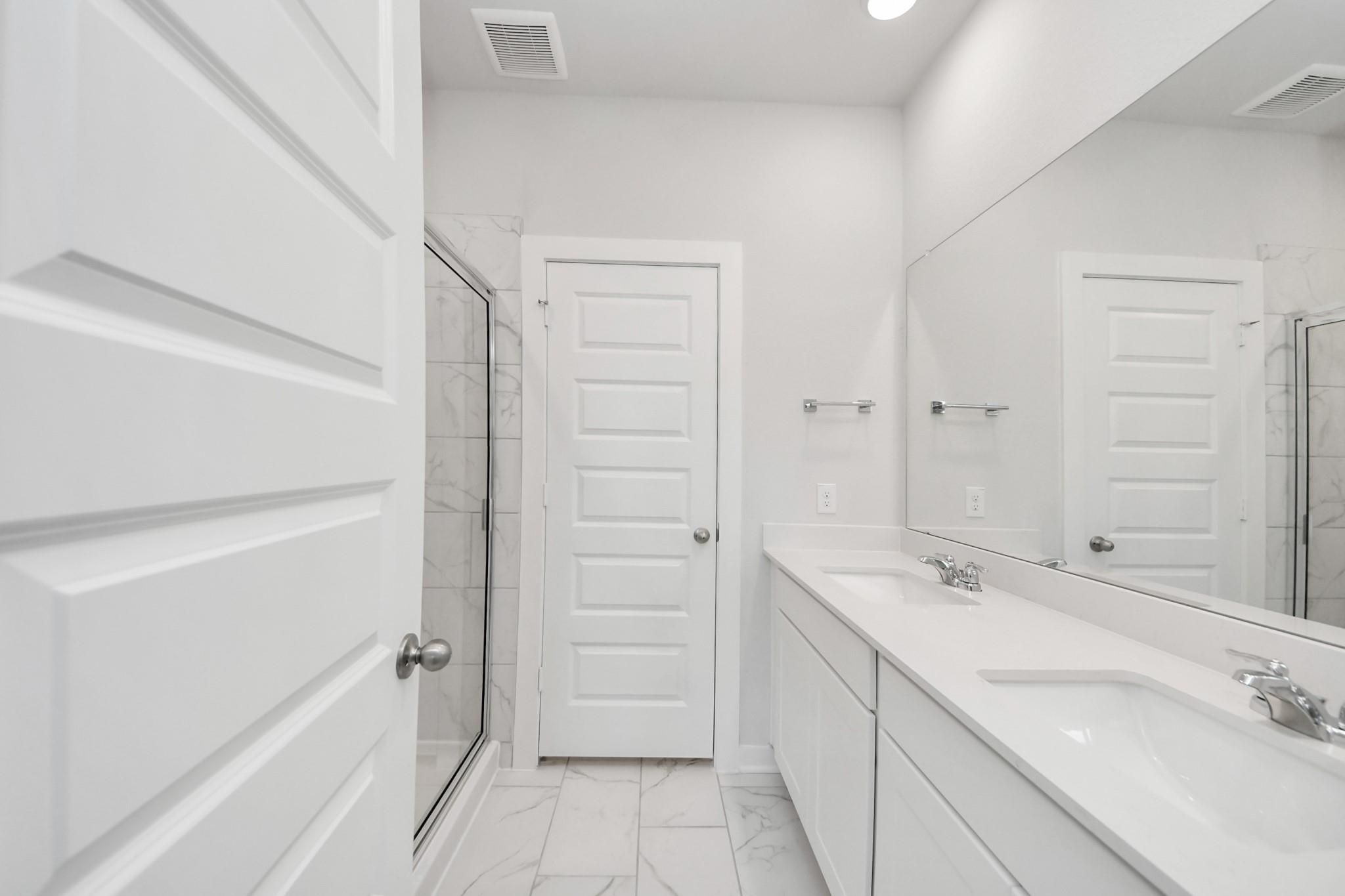 Modern bathroom with double vanity, white cabinetry, and glass-enclosed shower in The Sabine F plan at Liberty Estates.