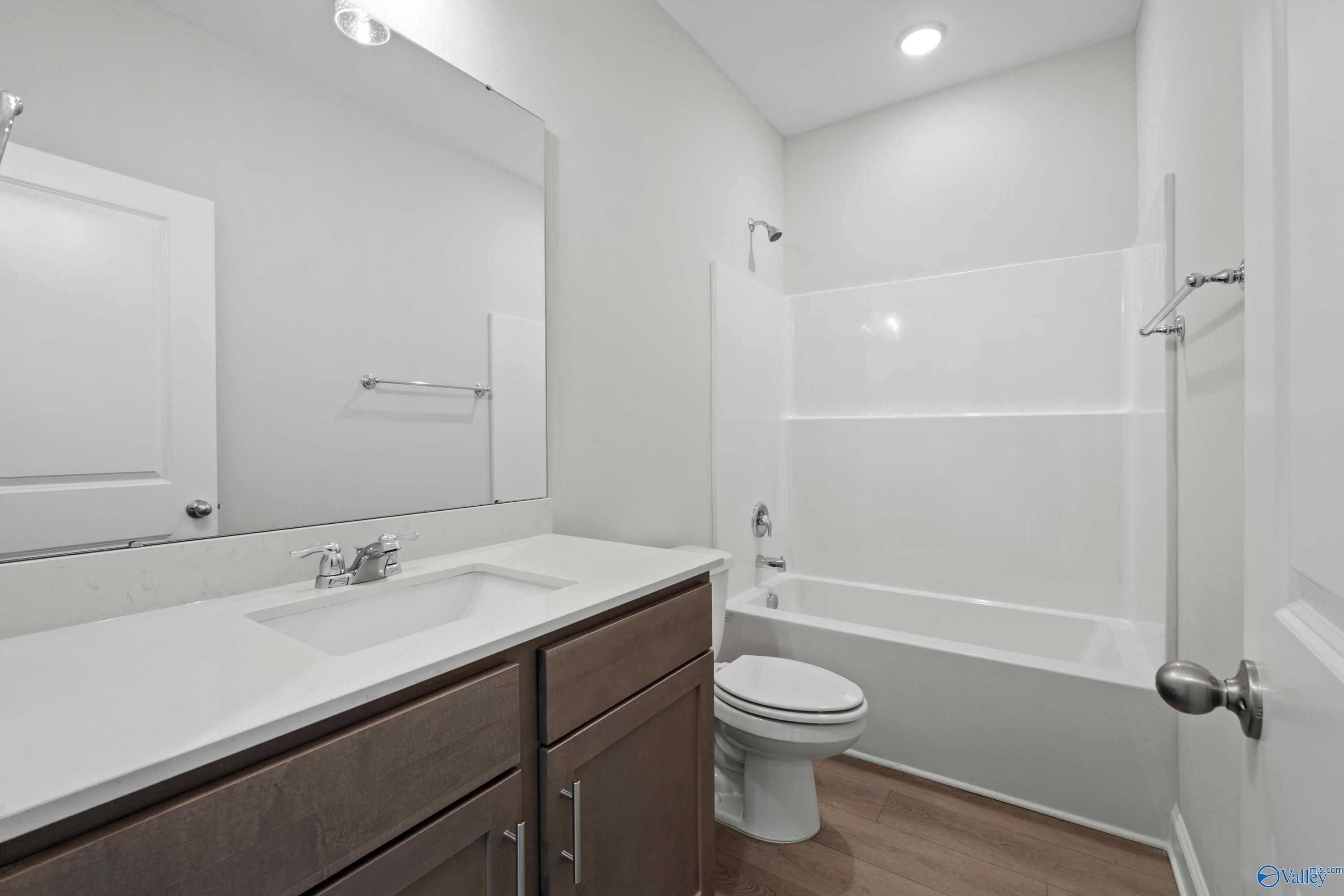 Modern bathroom with white tub-shower combo, brown vanity, and wood floors in Davidson Homes The Franklin C, Harvest, Alabama