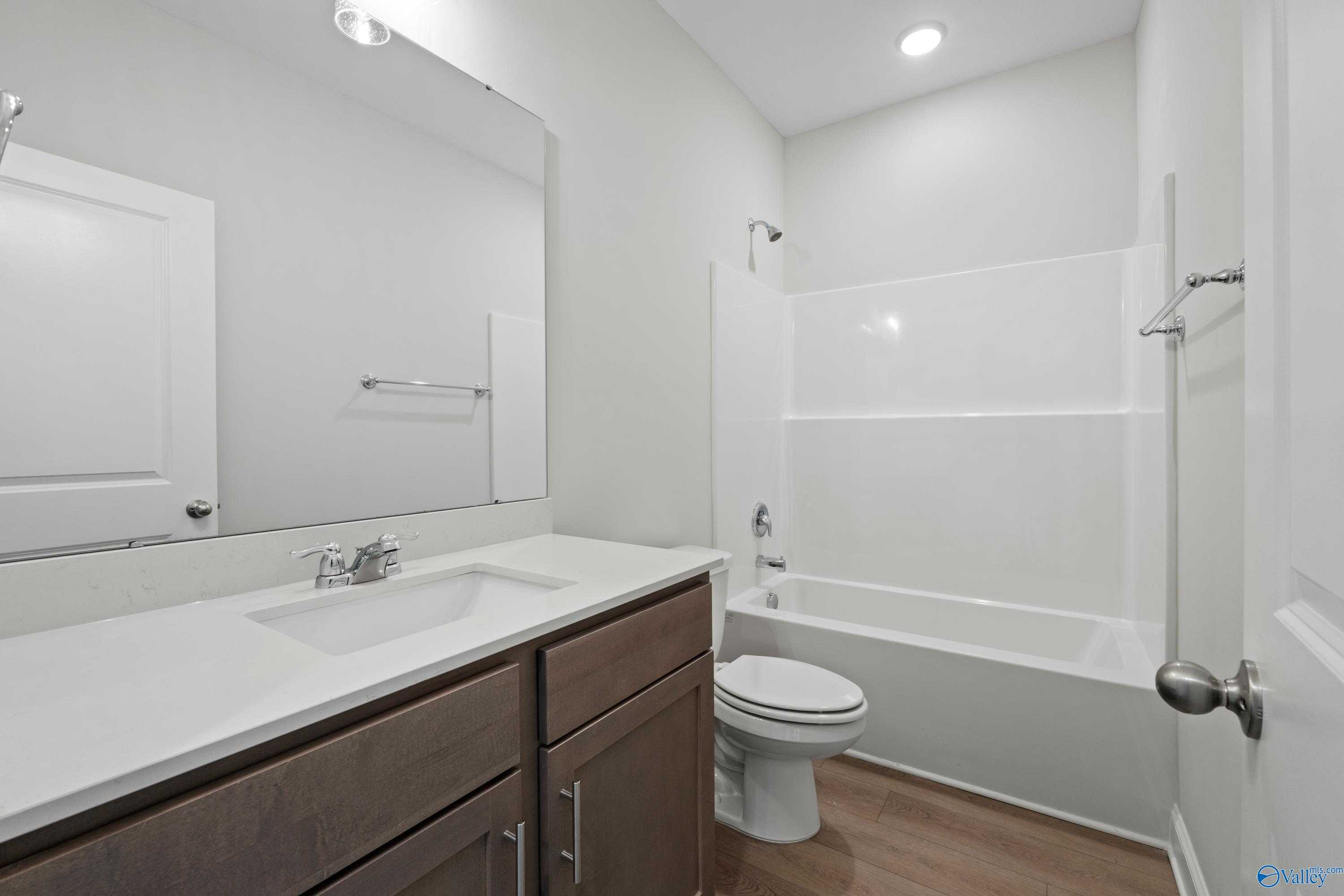 Modern bathroom with white tub-shower combo, brown vanity, and wood floors in Davidson Homes The Franklin C, Harvest, Alabama