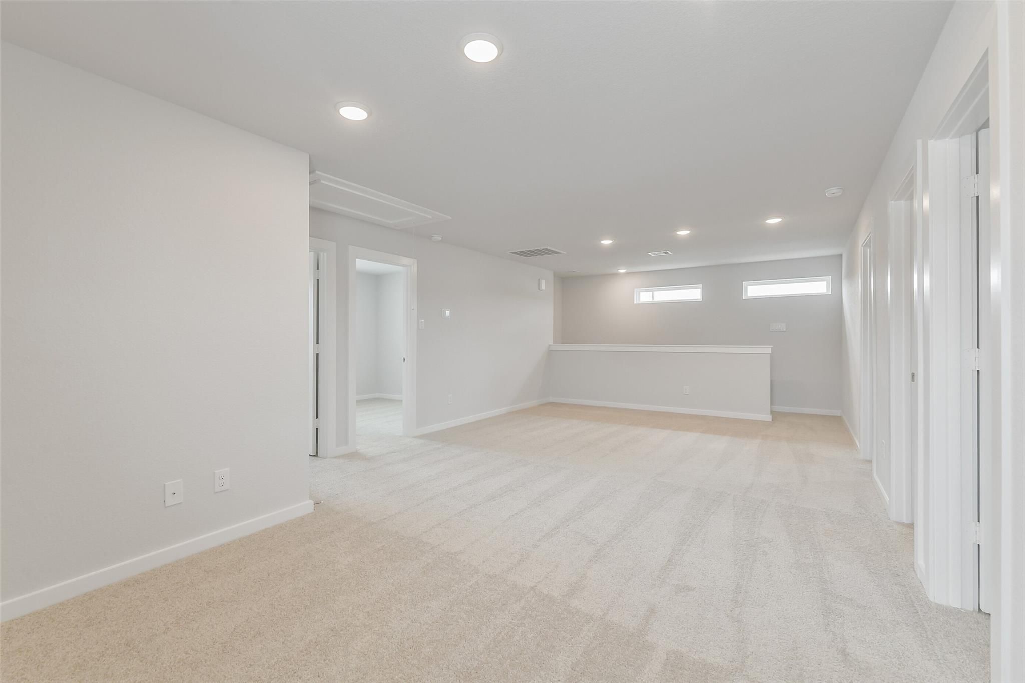 Spacious upstairs loft with beige carpet, white walls, recessed lights, and bedroom doors in 5-bed The Brazos E home, Cleveland, TX