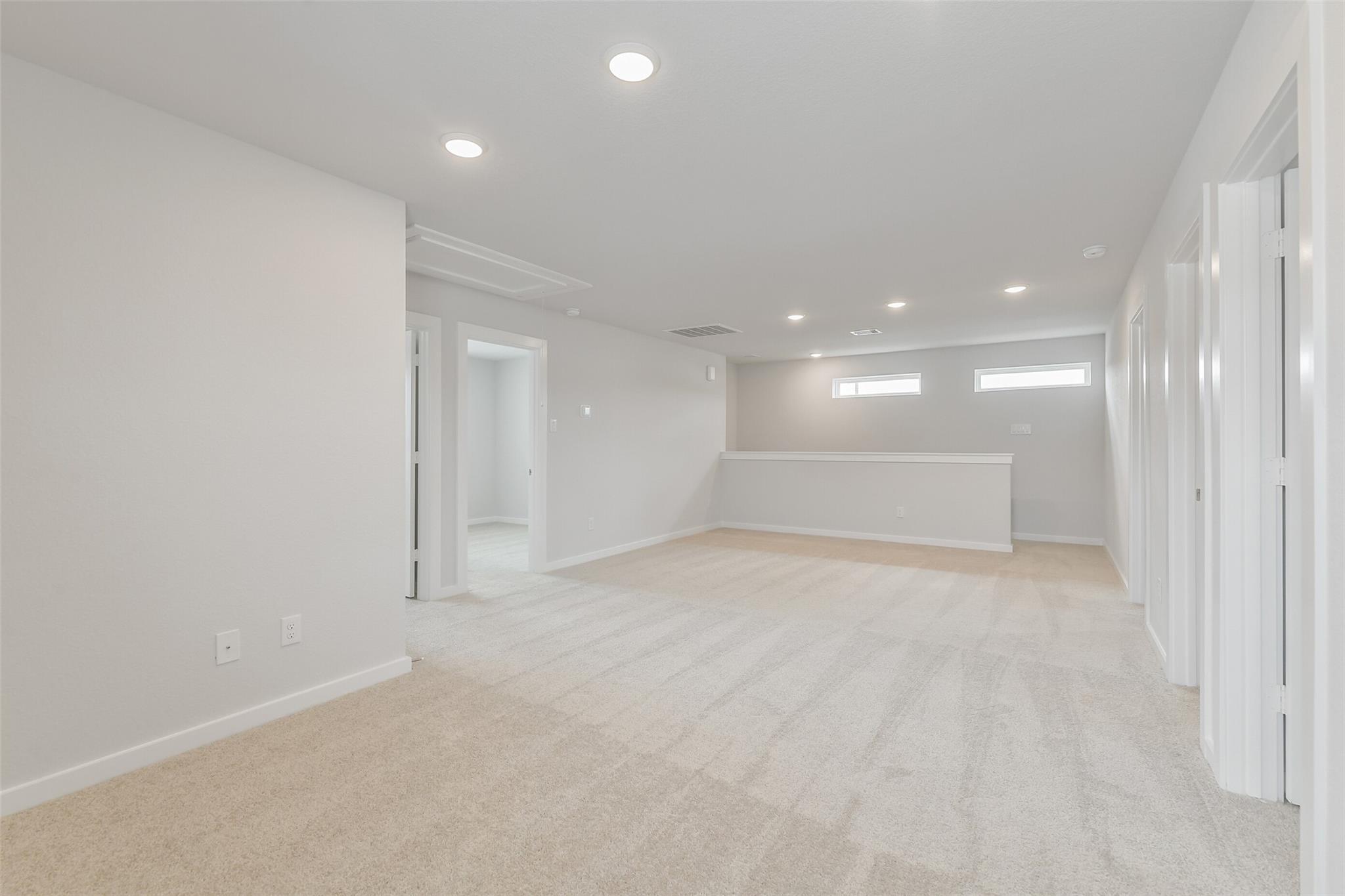 Spacious upstairs loft with beige carpet, white walls, recessed lights, and bedroom doors in 5-bed The Brazos E home, Cleveland, TX