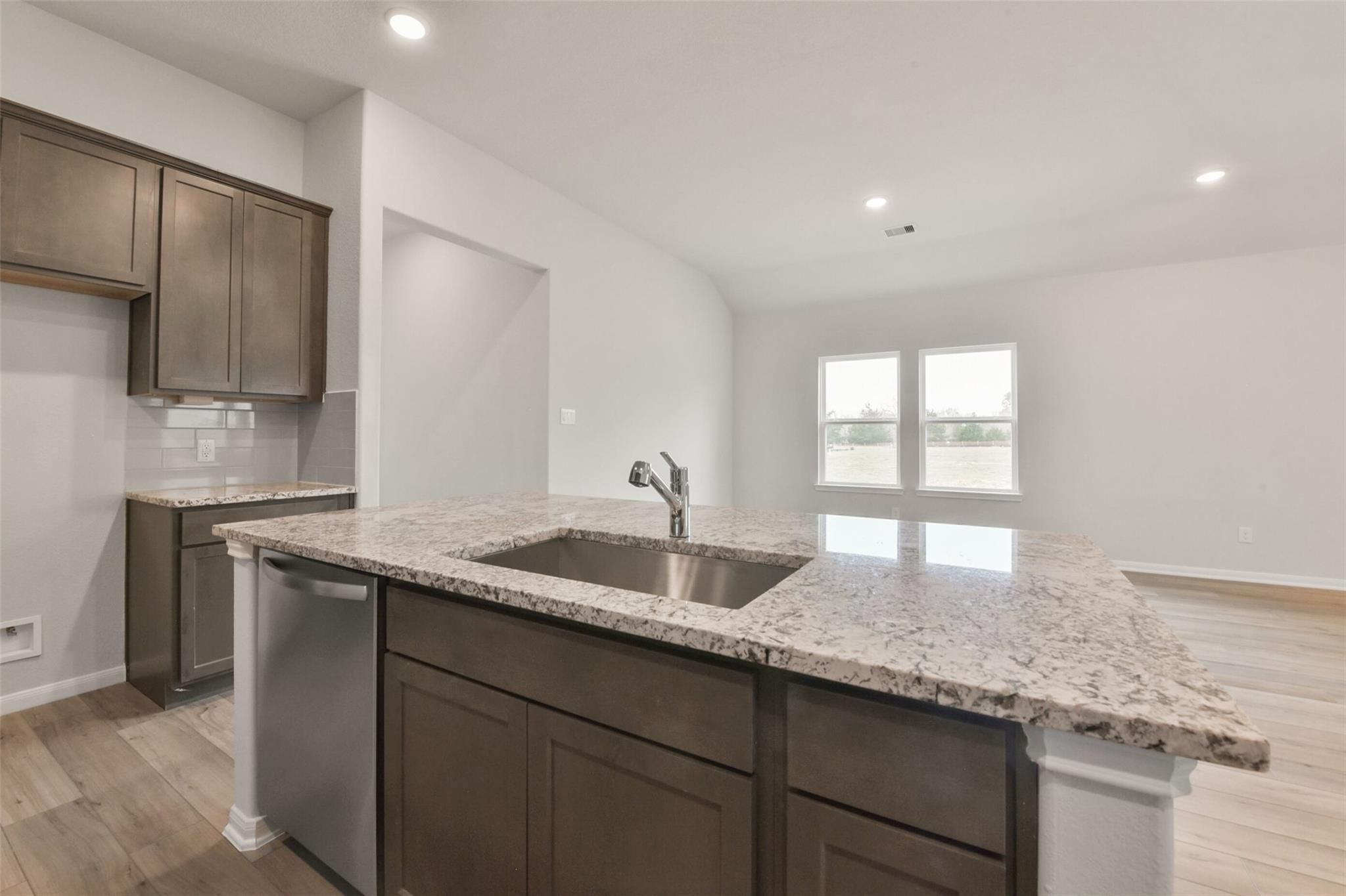 Modern kitchen with granite island sink, dark wood cabinets, stainless dishwasher in Davidson Homes The Laguna B, Magnolia, Texas
