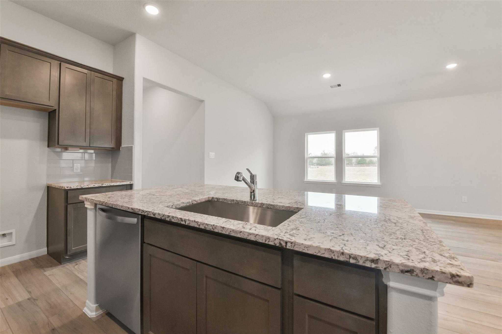 Modern kitchen with granite island, dark wood cabinets, stainless sink and dishwasher in The Laguna B, Davidson Homes, Magnolia TX