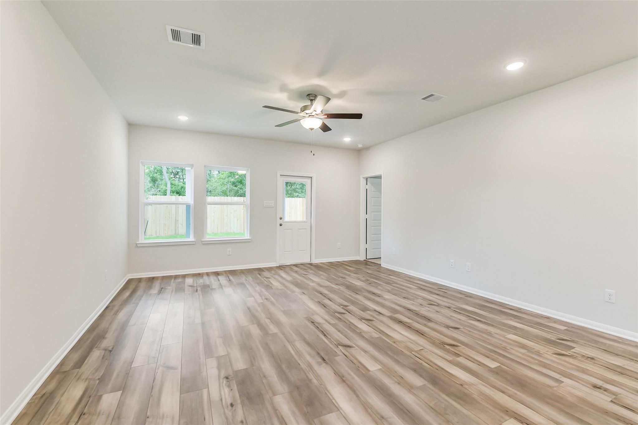 Spacious living room with hardwood floors, ceiling fan, and large windows in 5-bedroom Brazos F home, Conroe, Texas