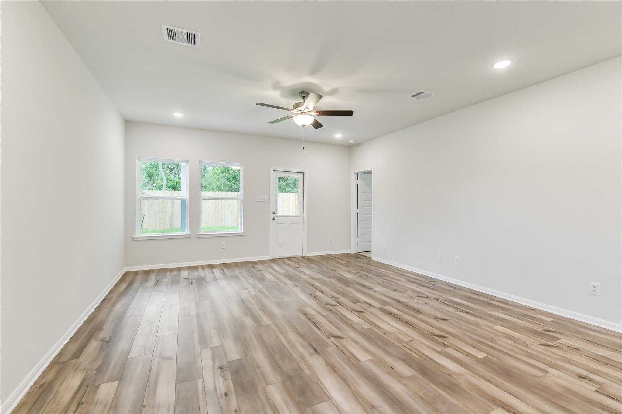 Spacious living room with hardwood floors, ceiling fan, and large windows in 5-bedroom Brazos F home, Conroe, Texas