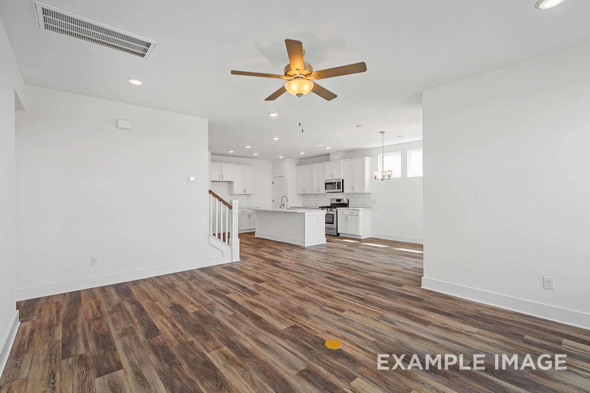 Spacious open-concept kitchen and living area in The Ash C with white cabinets, large island, wood flooring, and ceiling fan