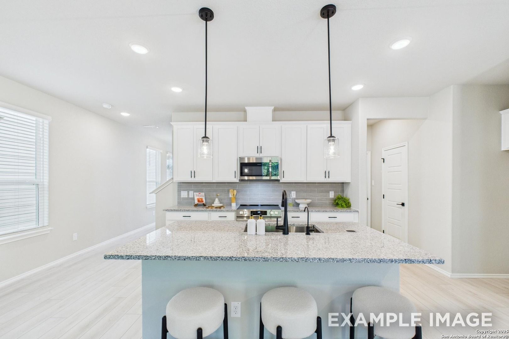 Modern kitchen with white cabinets, granite island, stainless appliances, and pendant lights in Davidson Homes Charlotte B, San Antonio