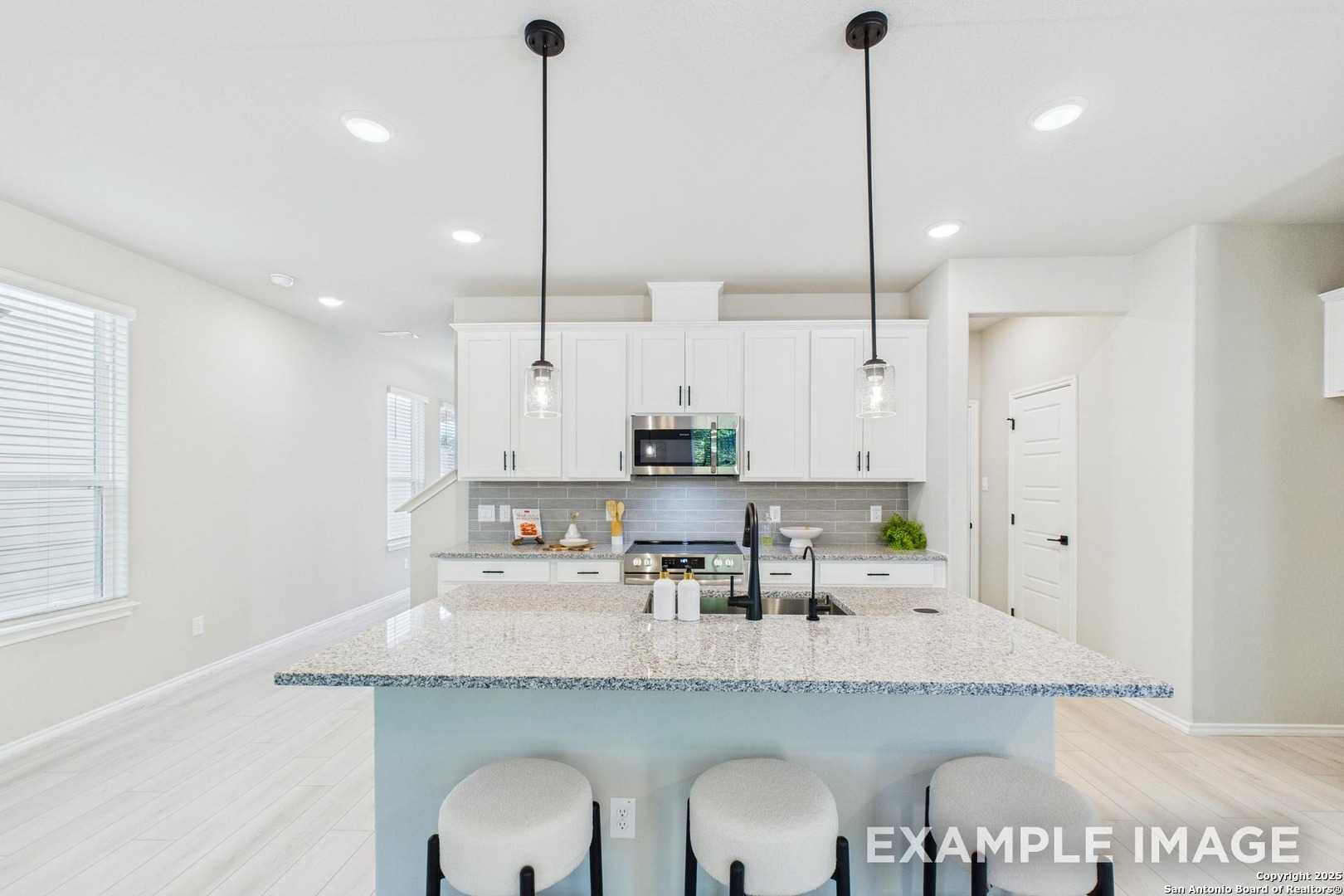 Modern kitchen with white cabinets, granite island, stainless appliances, pendant lights in Davidson Homes The Charlotte A, San Antonio