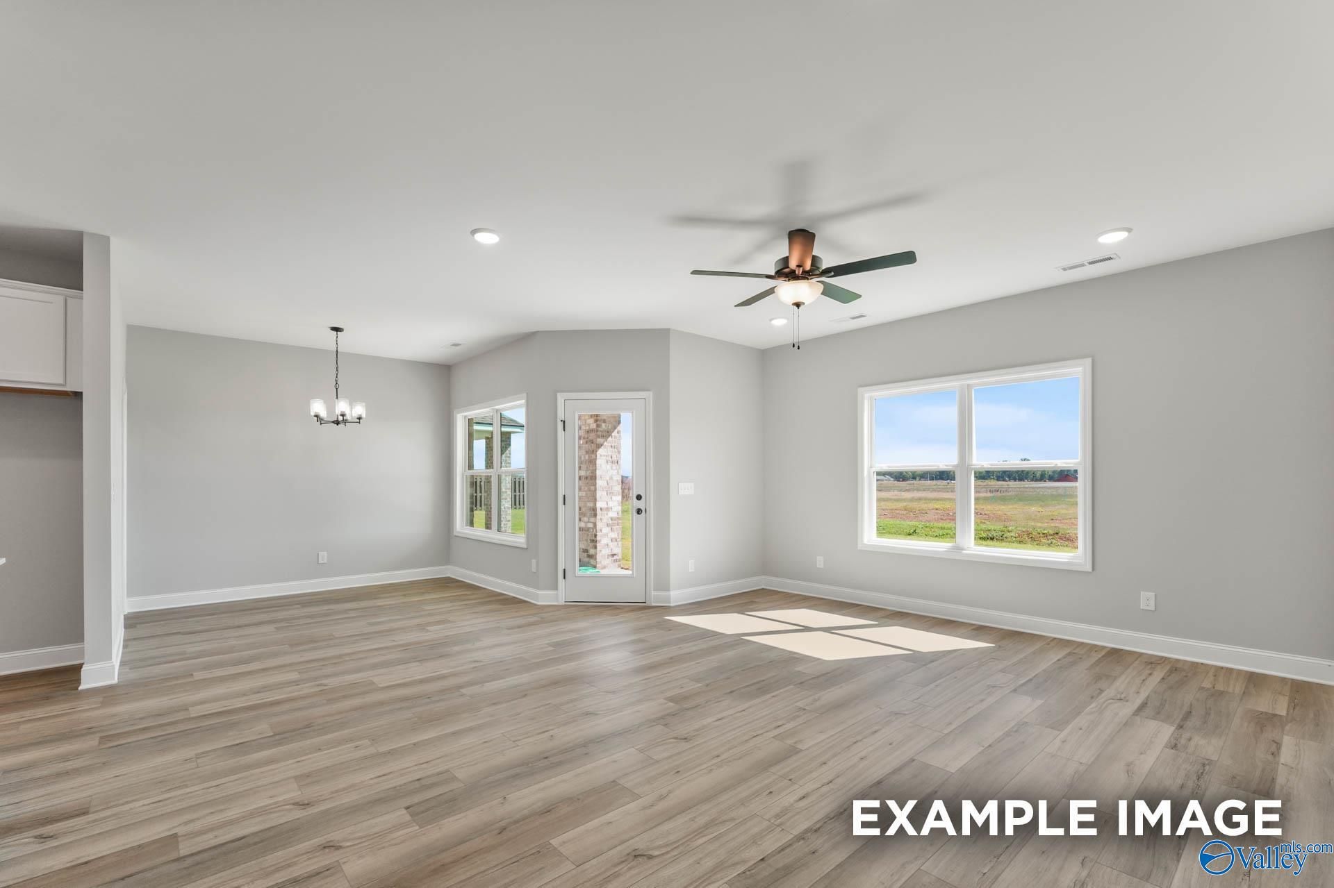 Bright open living room with hardwood floors, ceiling fan, and large windows overlooking fields in Davidson Homes The Daphne C, Athens, AL