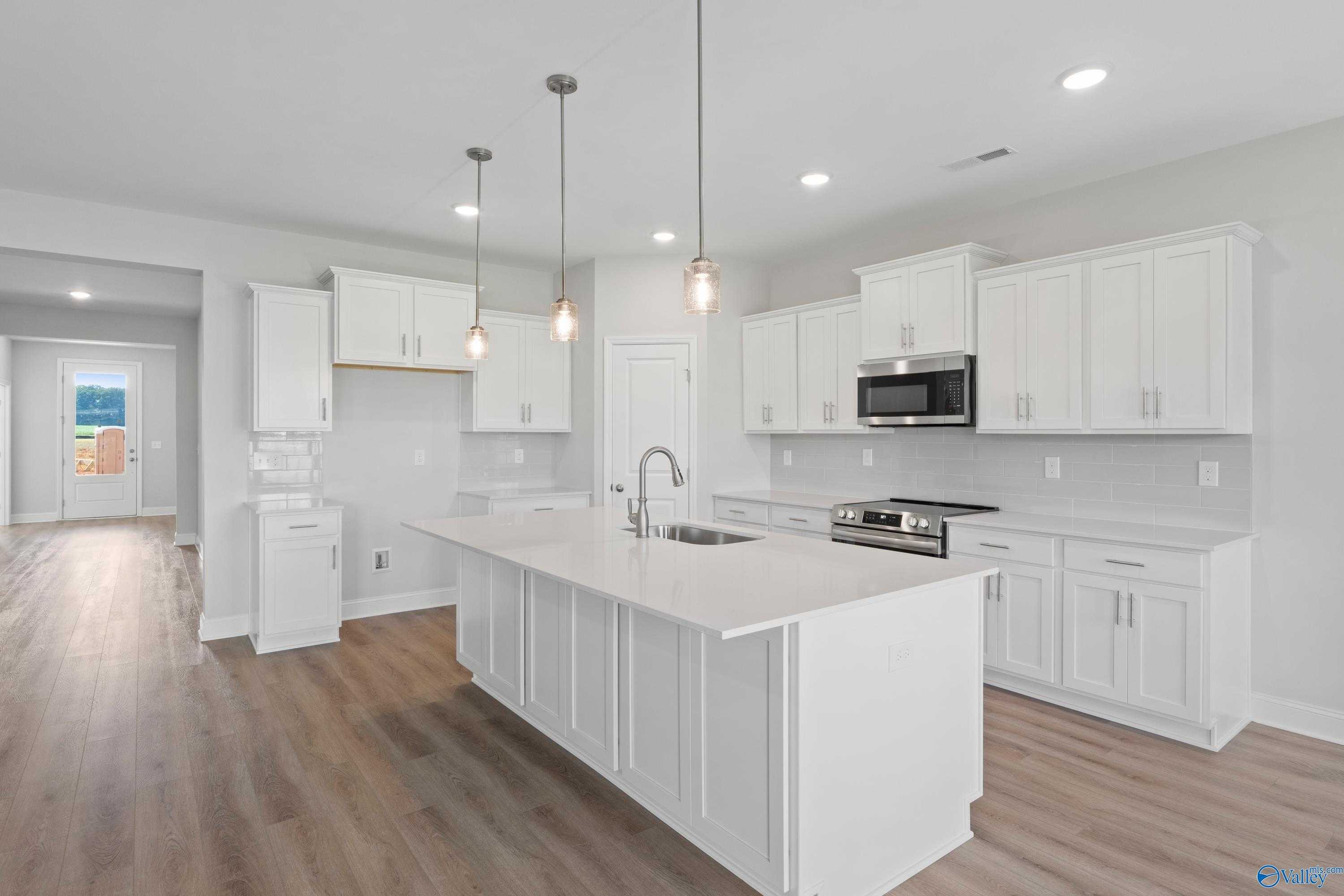 Modern white kitchen with large island, stainless appliances, pendant lights in open-concept The Harrison B home, Meridianville, Alabama