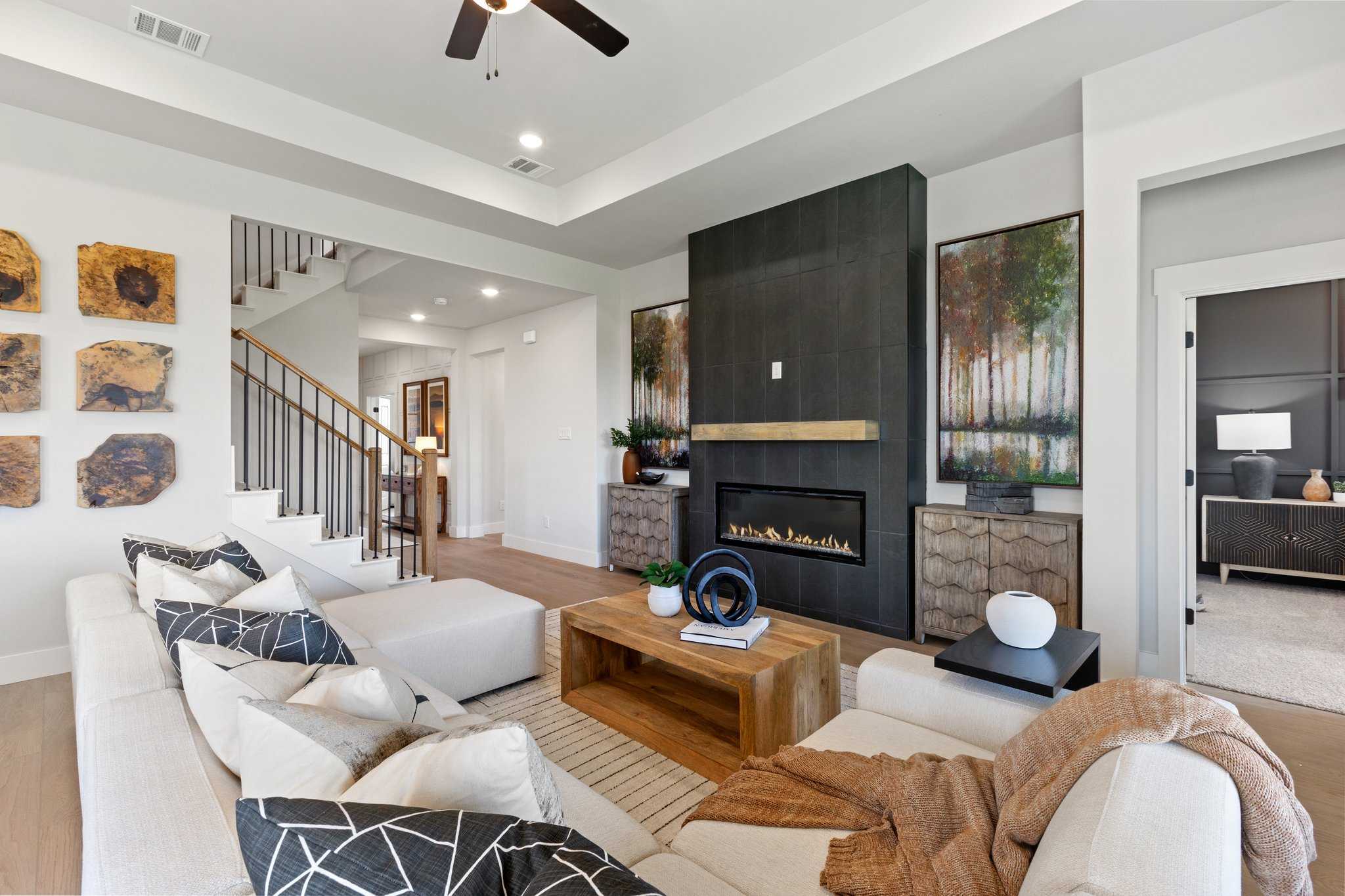 Open-concept living room at Mercer Meadows in Royse City TX featuring modern gas fireplace, staircase, and neutral sofas