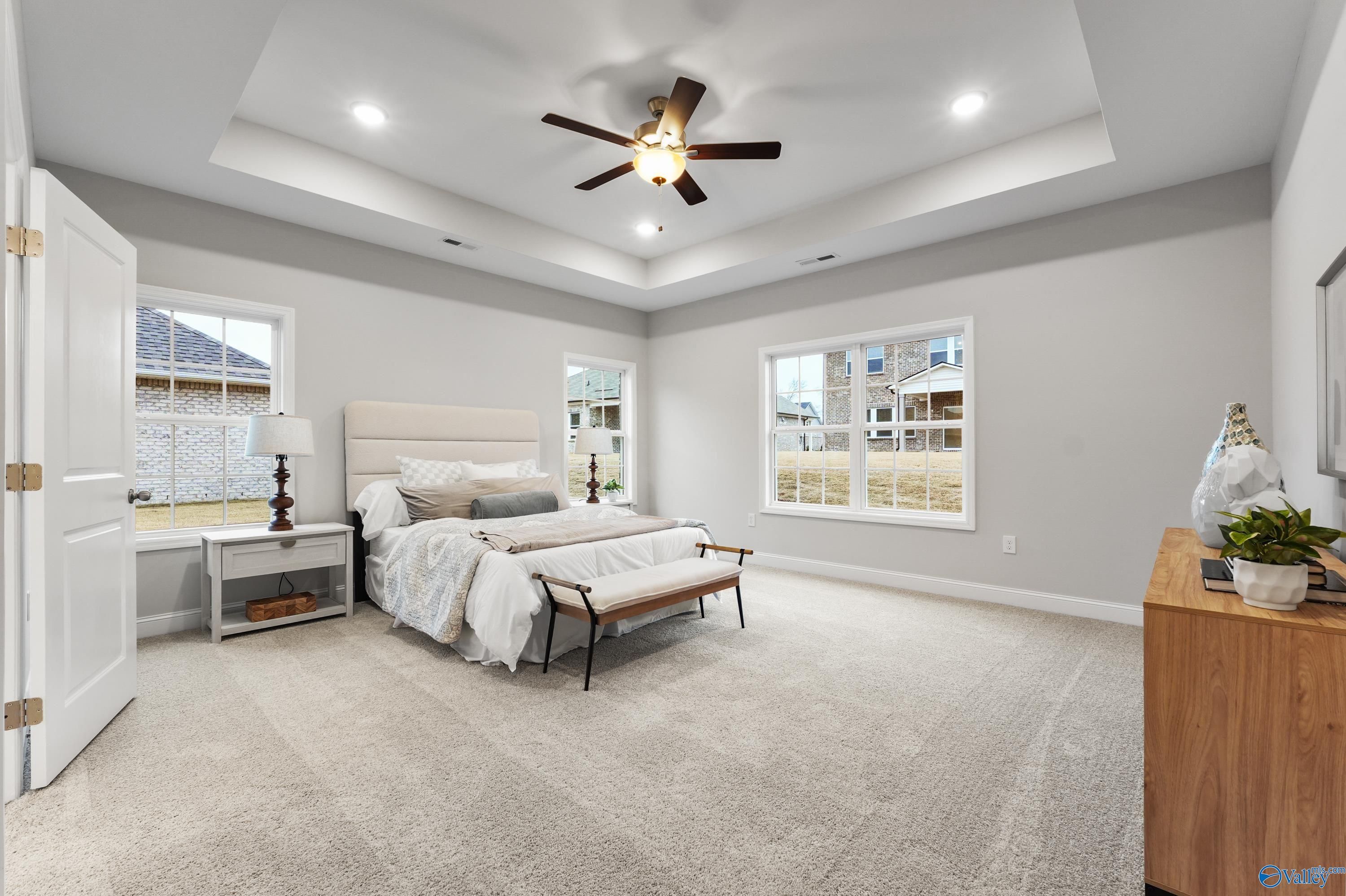 Spacious master bedroom with king bed, tray ceiling, ceiling fan, and large windows in Davidson Homes The Finleigh, Toney, Alabama