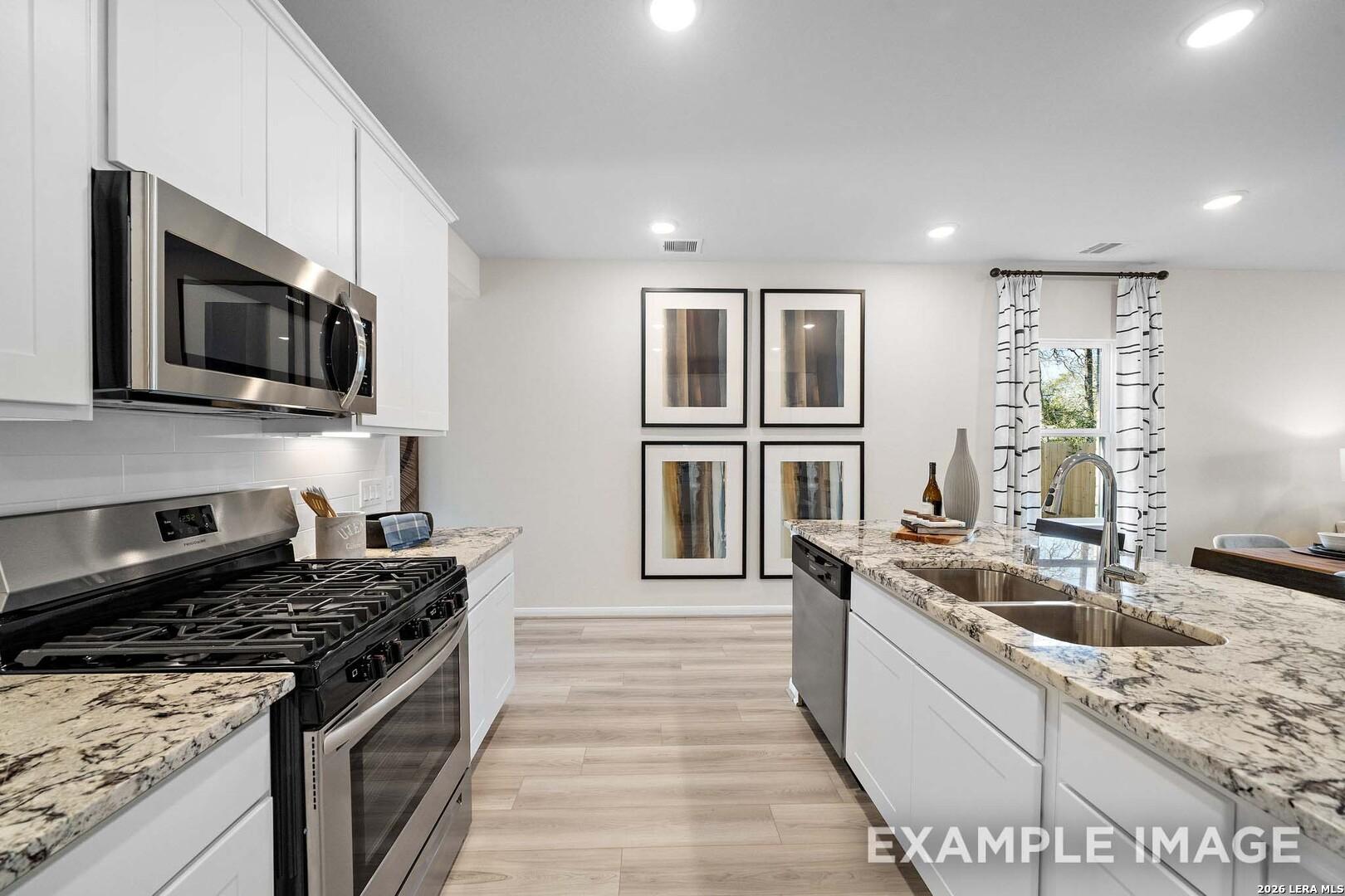 Modern kitchen with granite countertops, stainless appliances, and white cabinets in The San Marcos F, Rayburn Valley, TX.