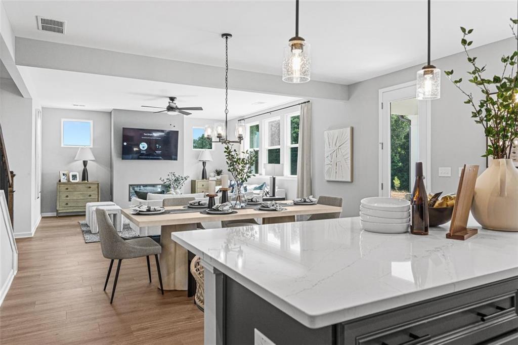 Open-concept dining and living space with quartz kitchen island, set table, and wall-mounted TV in Davidson Homes The Hickory B, Hoschton, GA
