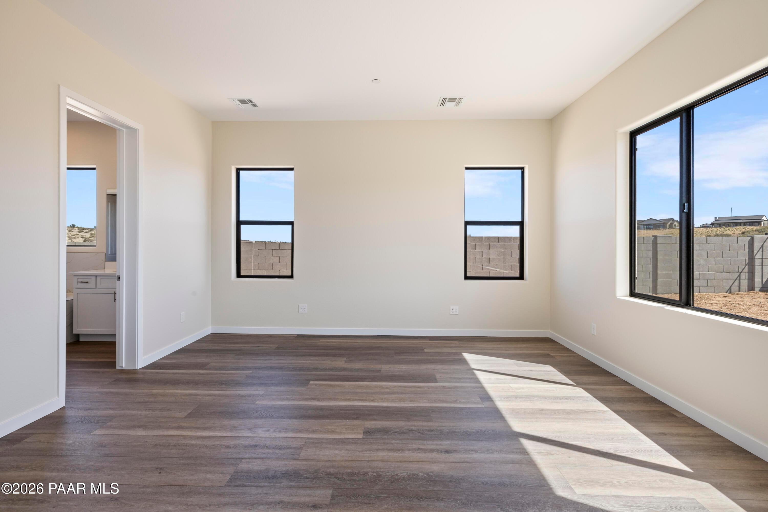 Bright bedroom with hardwood floors, large black-framed windows, desert view, and en-suite bath in Davidson Homes Soleil E, Prescott AZ
