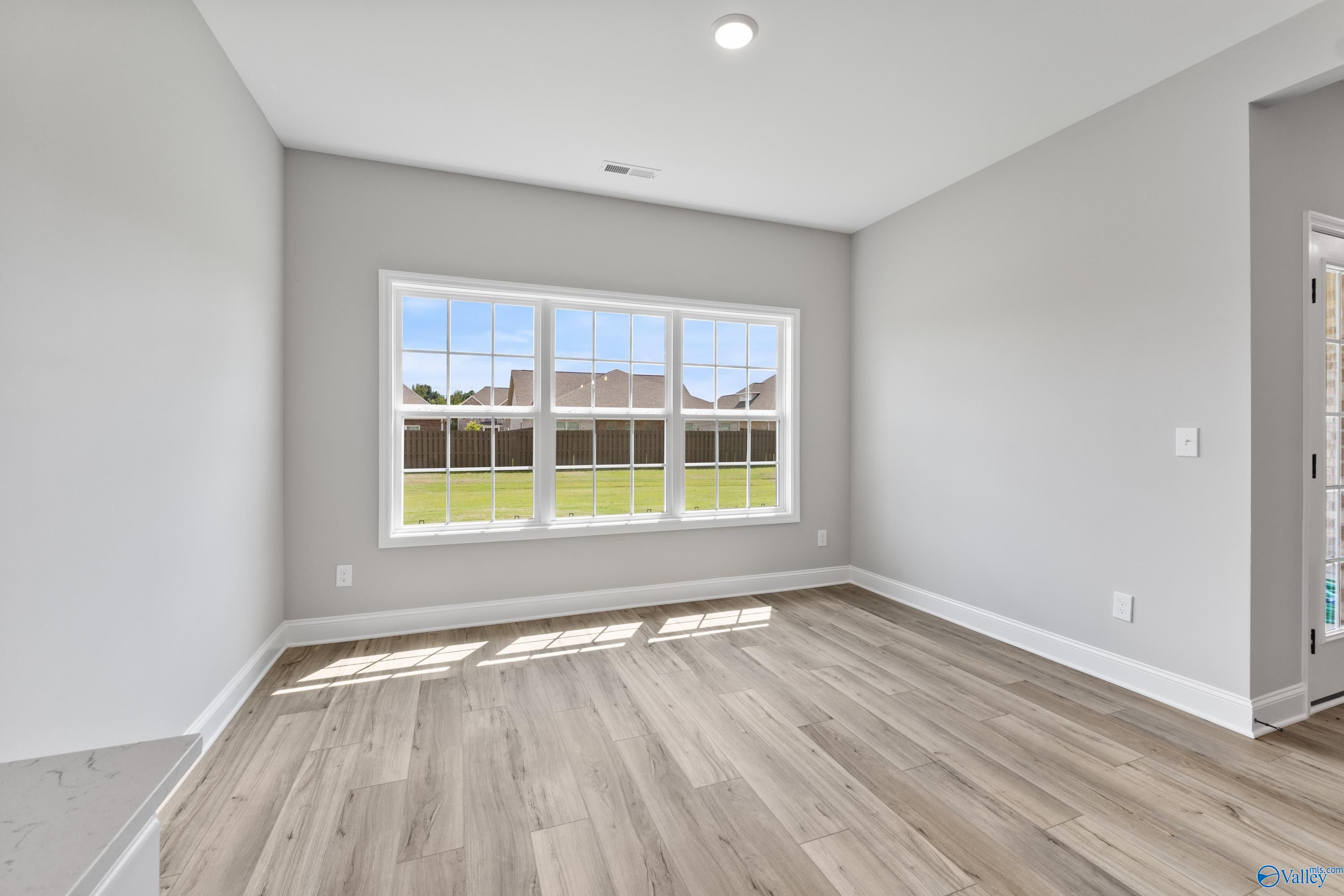 Bright bonus room with large windows and light wood floors overlooking lush green yard in Davidson Homes Montgomery B With Bonus, Toney, Alabama