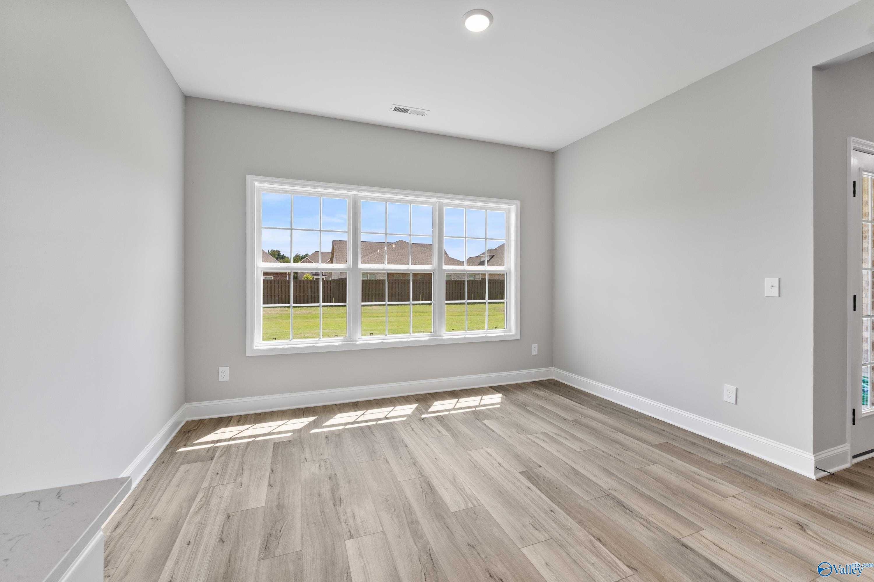 Bright bonus room with large windows and light wood floors overlooking lush green yard in Davidson Homes Montgomery B With Bonus, Toney, Alabama