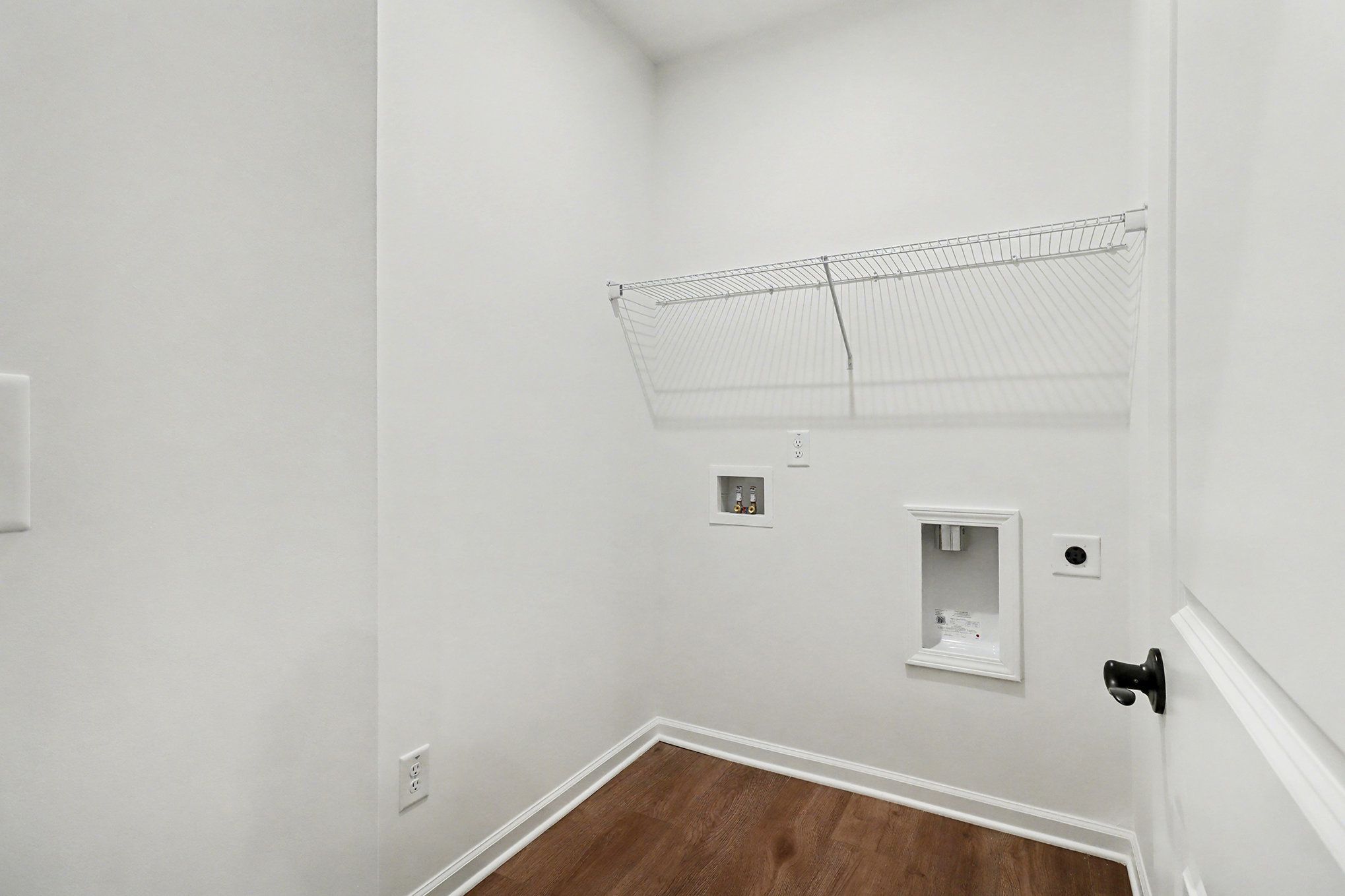Bright laundry room with utility sink, wire shelving, and beige walls in Davidson Homes The Daphne B, Kelly Preserve, Loganville, Georgia