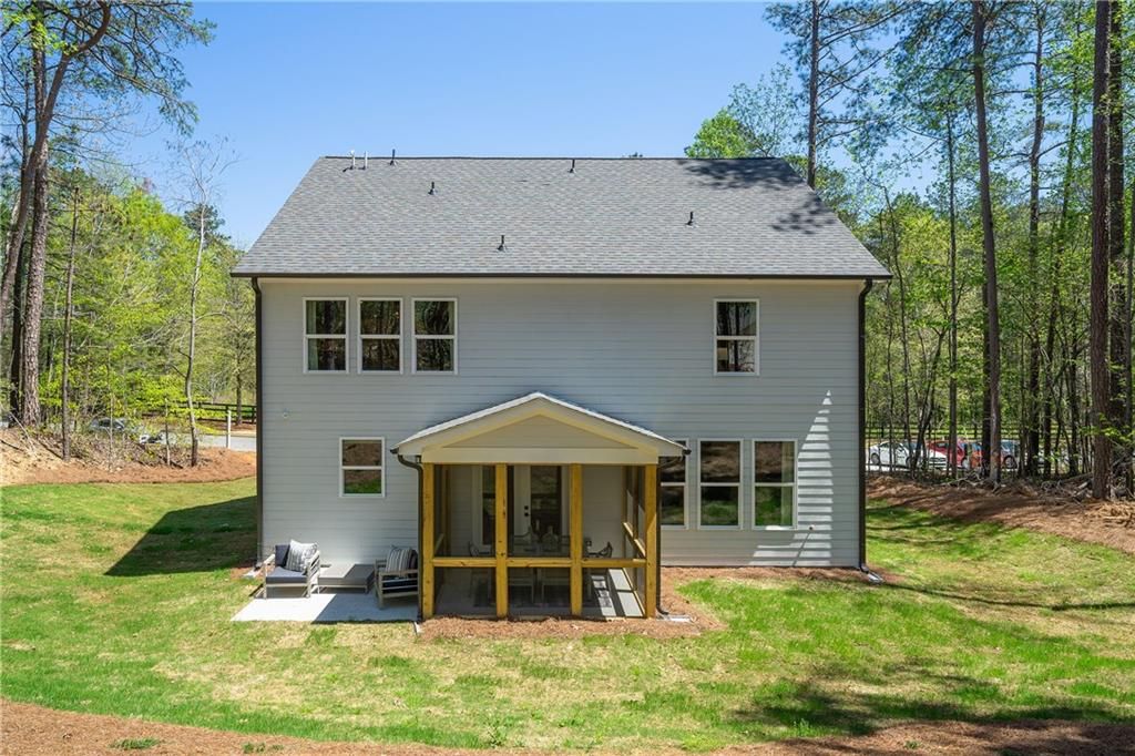 Rear view of two-story Willow B home with covered porch, lush green yard, and surrounding pines in Riverwood, Dallas, Georgia