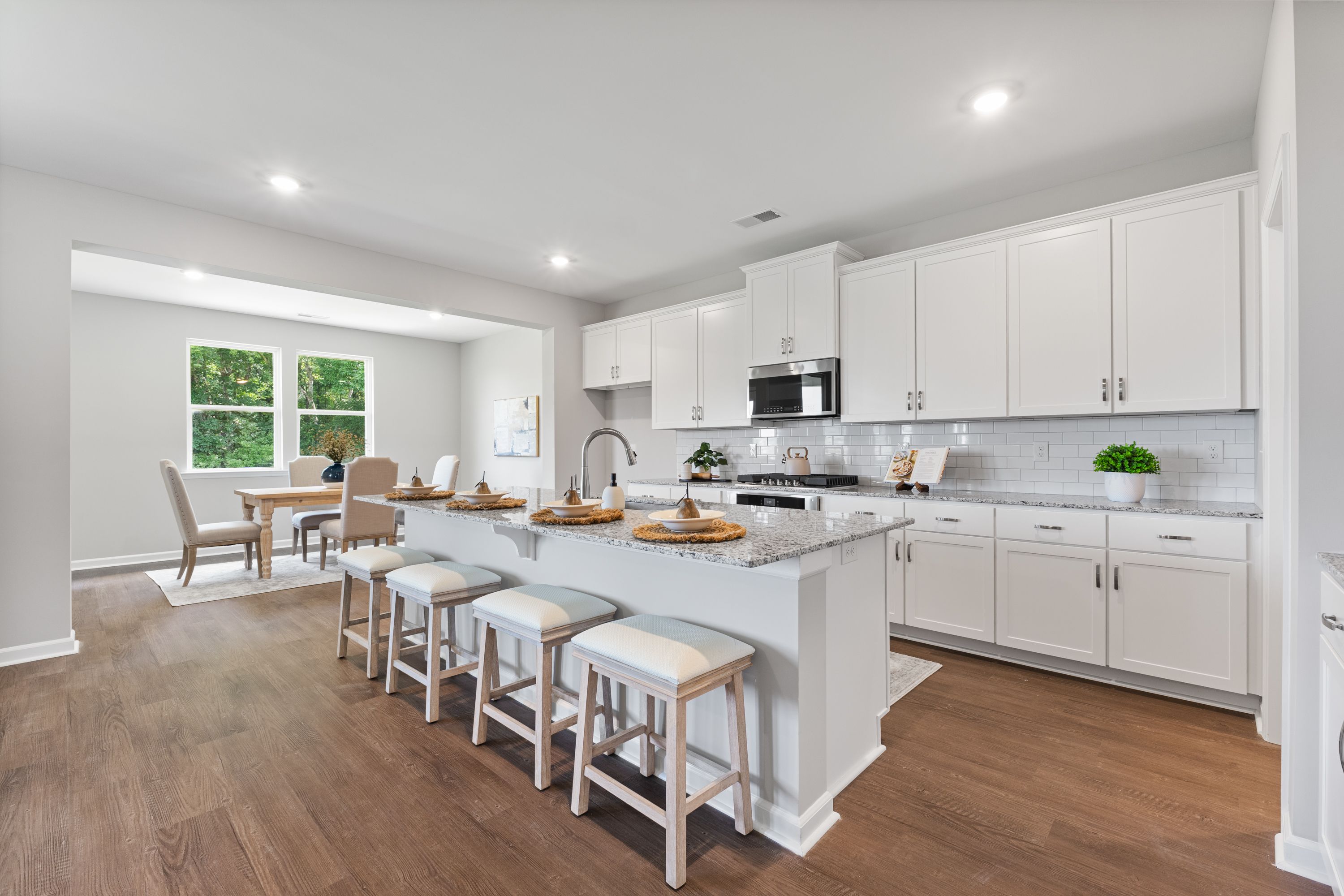 Spacious open-concept kitchen in The Avalon E with white shaker cabinets, large quartz island, bar stools, and adjacent dining area