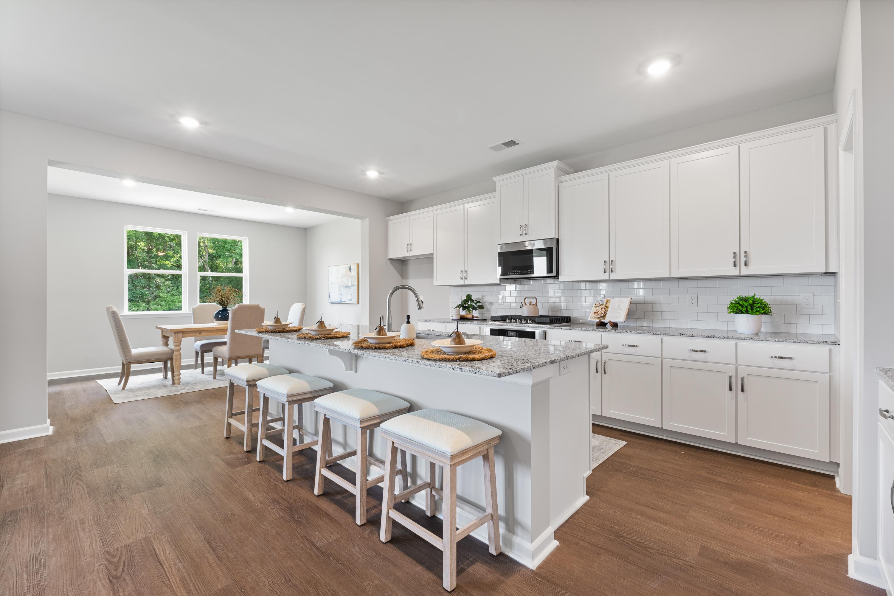 Spacious gourmet kitchen in The Avalon D featuring white shaker cabinets, quartz island with bar stools, and open dining nook