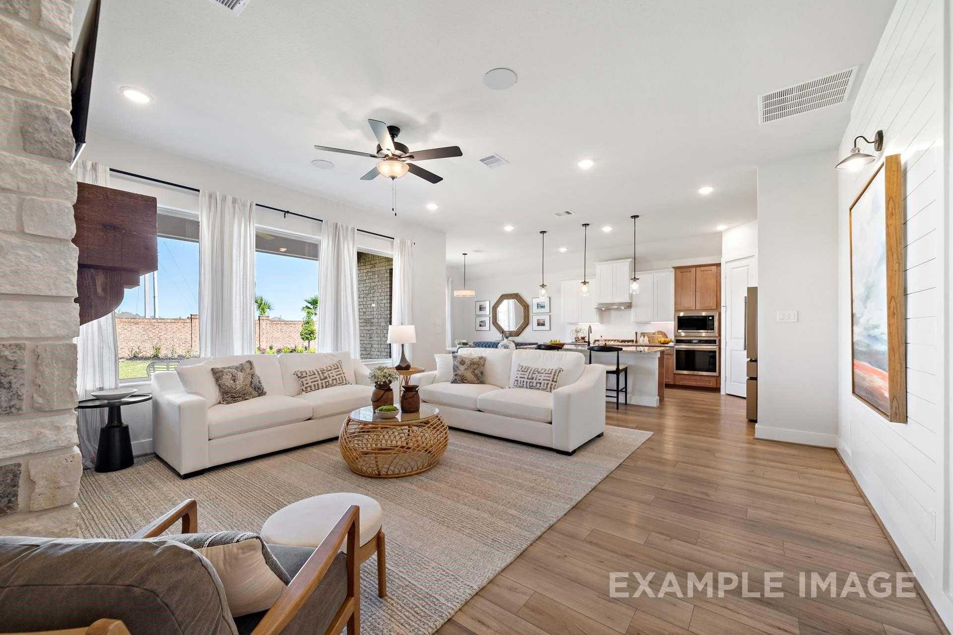Open-concept living room with stone fireplace, white sofas, and adjoining white kitchen in Davidson Homes The Edward A, Lago Mar, Texas City